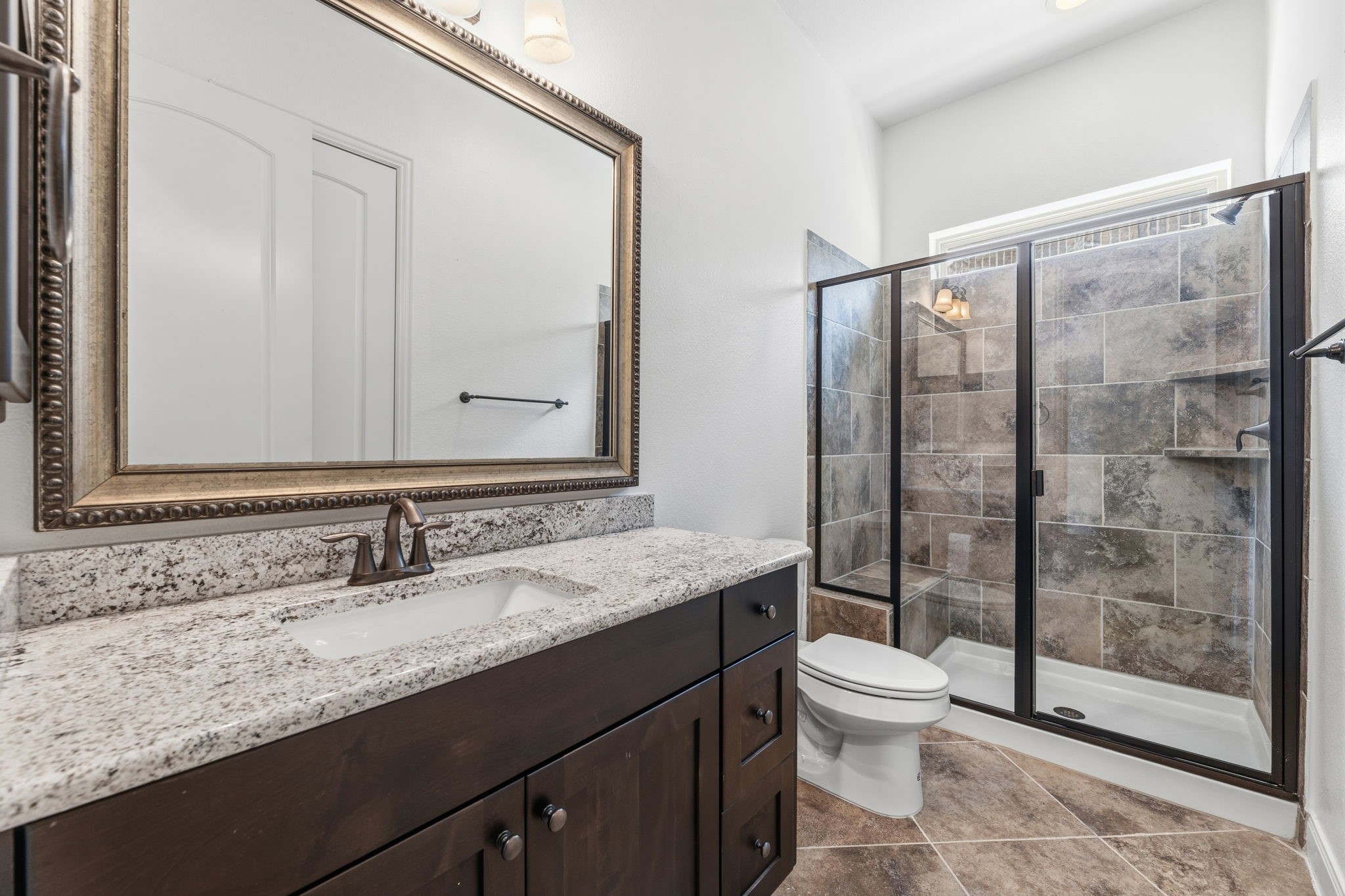 Bathroom featuring a granite countertop with a large, framed mirror and a glass-enclosed shower. Bathroom featuring a granite countertop with a large, framed mirror and a glass-enclosed shower.
