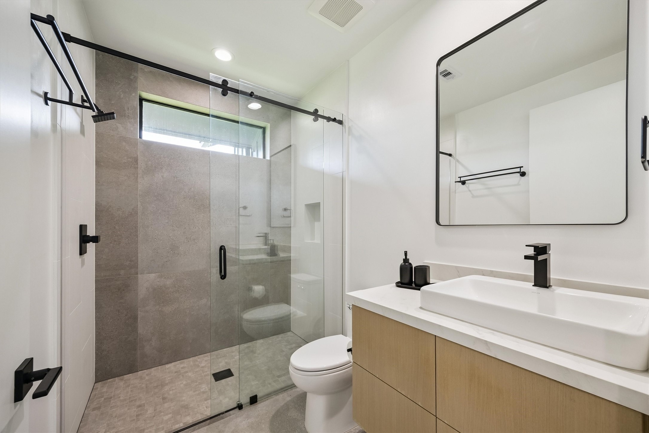 Beautifully coordinated finishes, a glass-enclosed shower, and sleek black fixtures give this guest bathroom a fresh, sophisticated aesthetic.