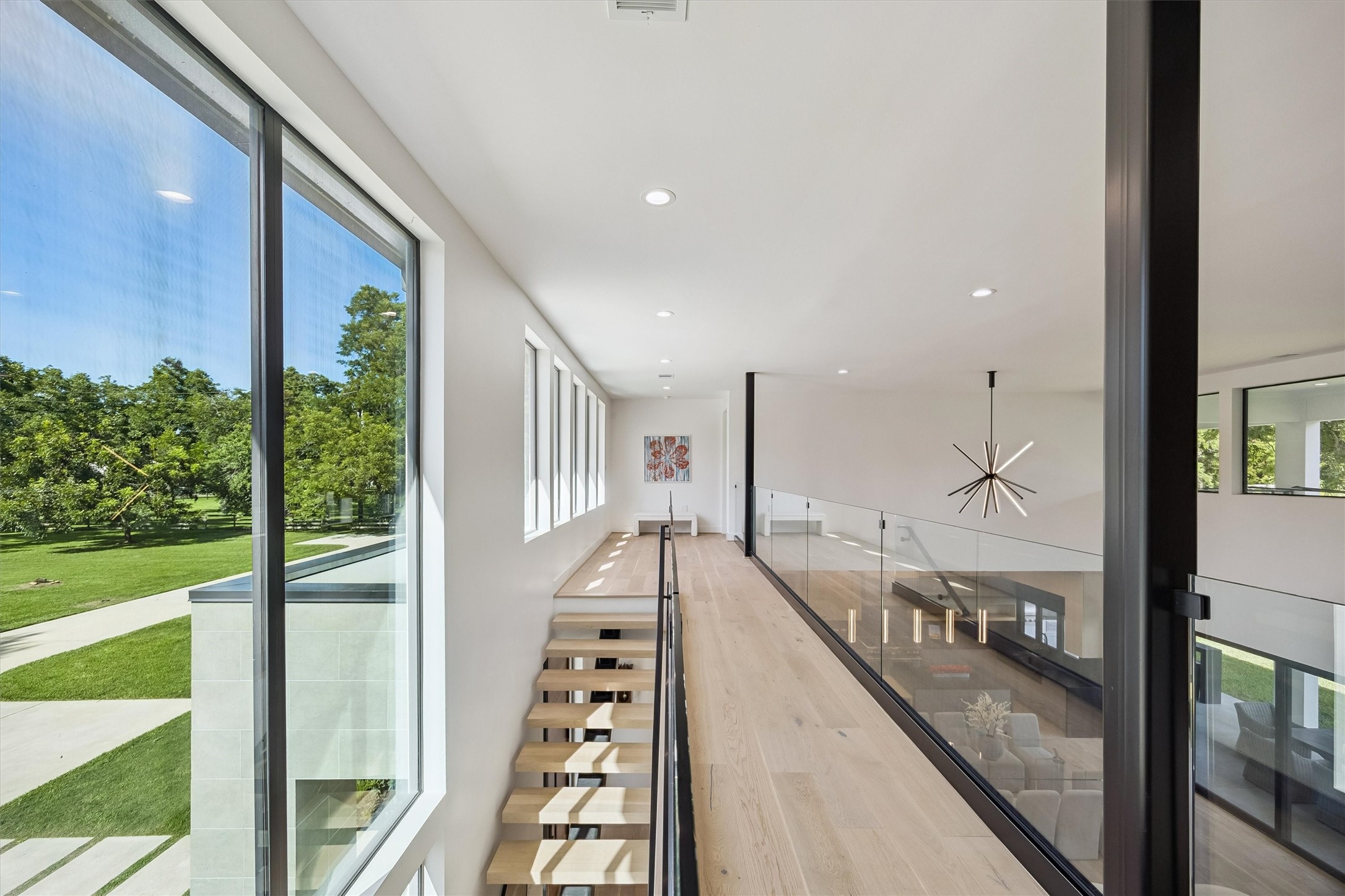 A spectacular gallery overlooks the grand living spaces below, where expansive windows, sleek glass railings, and beautiful architectural details celebrate the home's extraordinary openness.