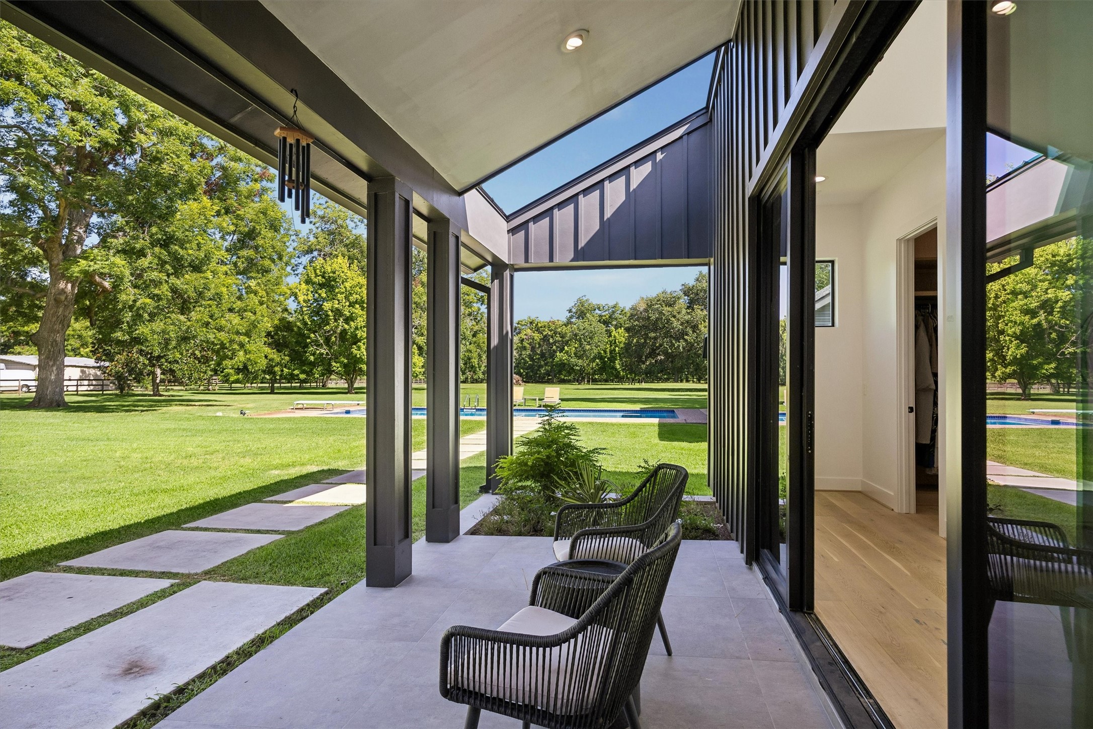 Floor-to-ceiling glass and a sheltered sitting area invite the surrounding landscape into view, creating a peaceful transition between the residence and its beautifully maintained outdoor spaces.