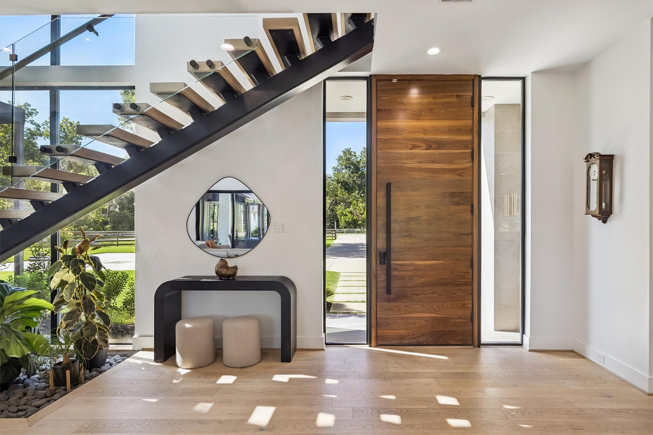 Elegant entryway featuring a striking floating staircase, sleek wooden door, and modern decor, complemented by large windows that flood the space with natural light. Elegant entryway featuring a striking floating staircase, sleek wooden door, and modern decor, complemented by large windows that flood the space with natural light.