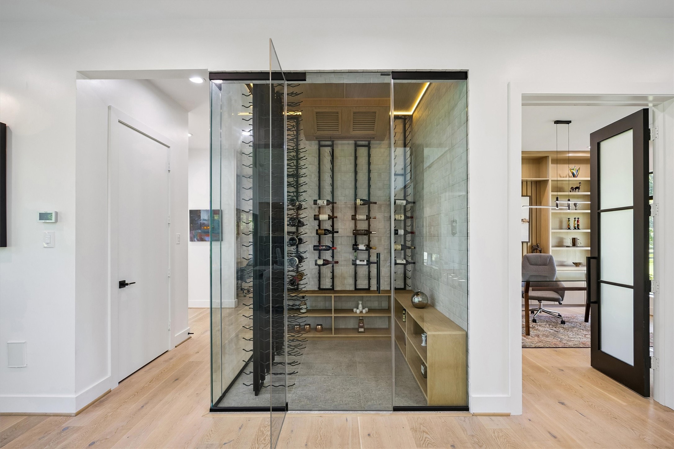 A sophisticated glass-enclosed wine display introduces an unexpected touch of luxury, combining architectural transparency, illuminated storage, and a striking presentation for a treasured collection.