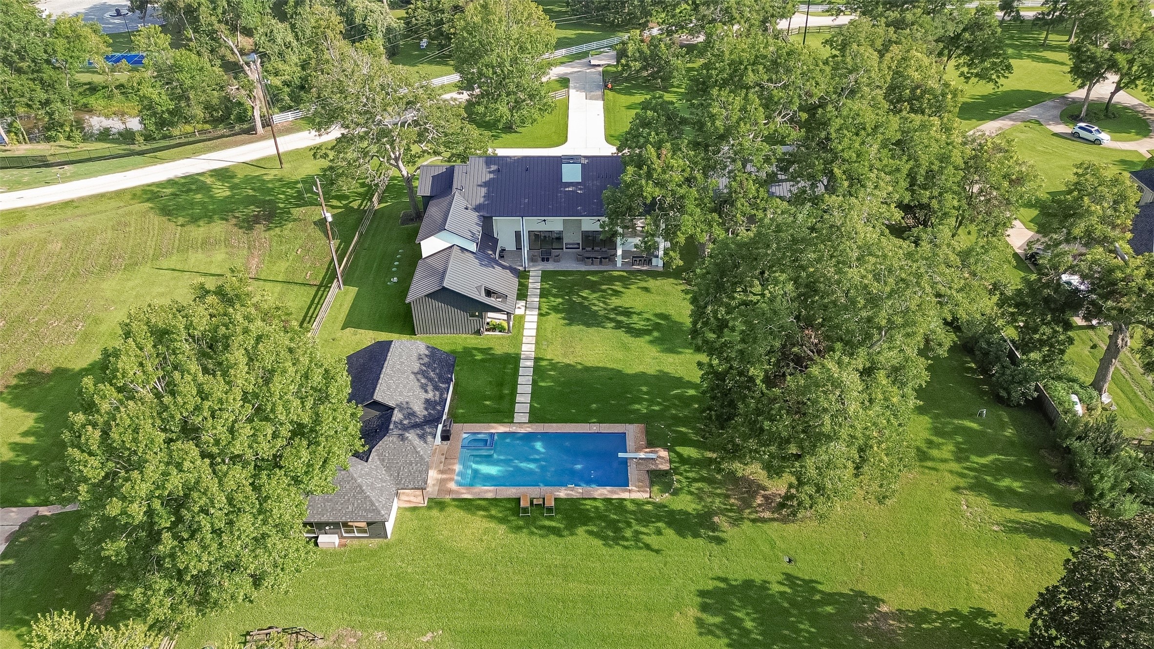 An elevated perspective captures the estate's exceptional outdoor amenities, including the inviting swimming pool, detached structures, and expansive grounds surrounded by mature trees.
