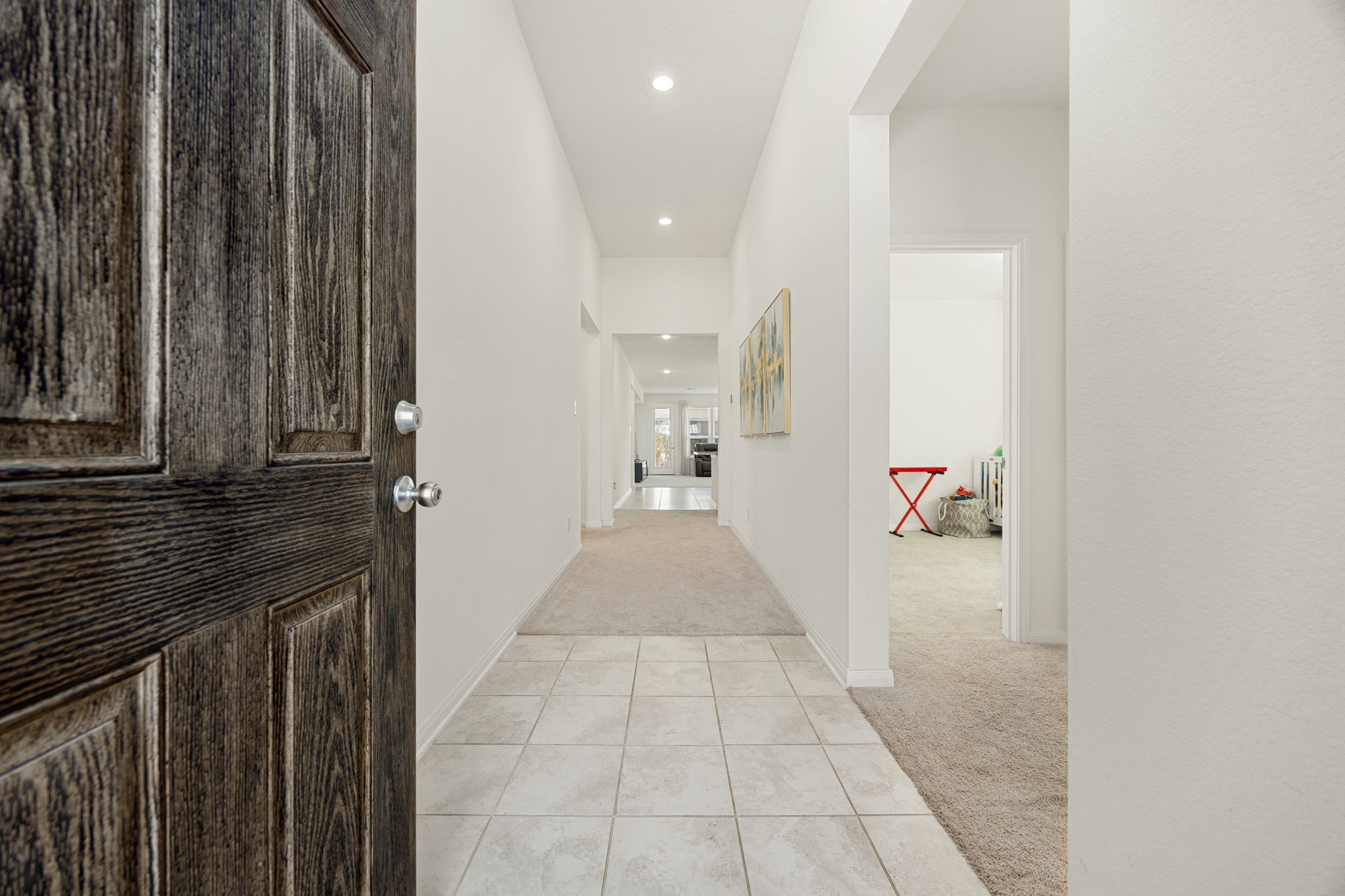 Step inside a bright and airy foyer featuring neutral tile flooring, high ceilings with recessed lighting, and a long hallway that leads seamlessly into the main living spaces.