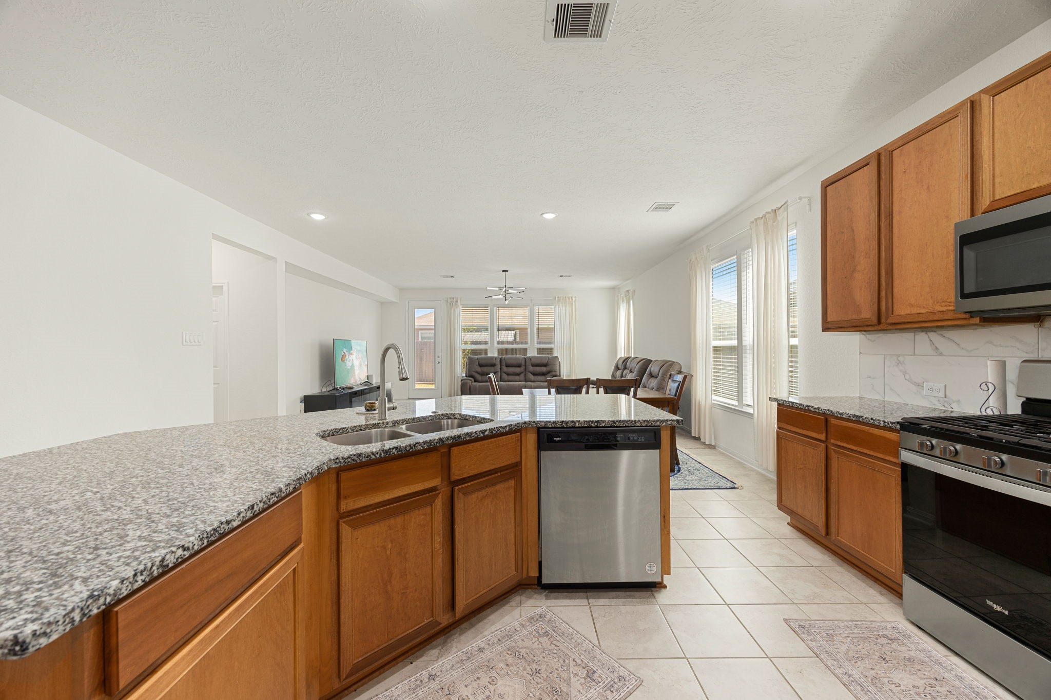 The oversized, uniquely angled kitchen island serves as the central focal point of the main living pavilion. This expansive workspace features durable granite countertops, an integrated double-bowl stainless steel sink with a goose-neck faucet, and a built-in stainless steel dishwasher, all while keeping the chef fully connected to the adjacent dining and living areas.