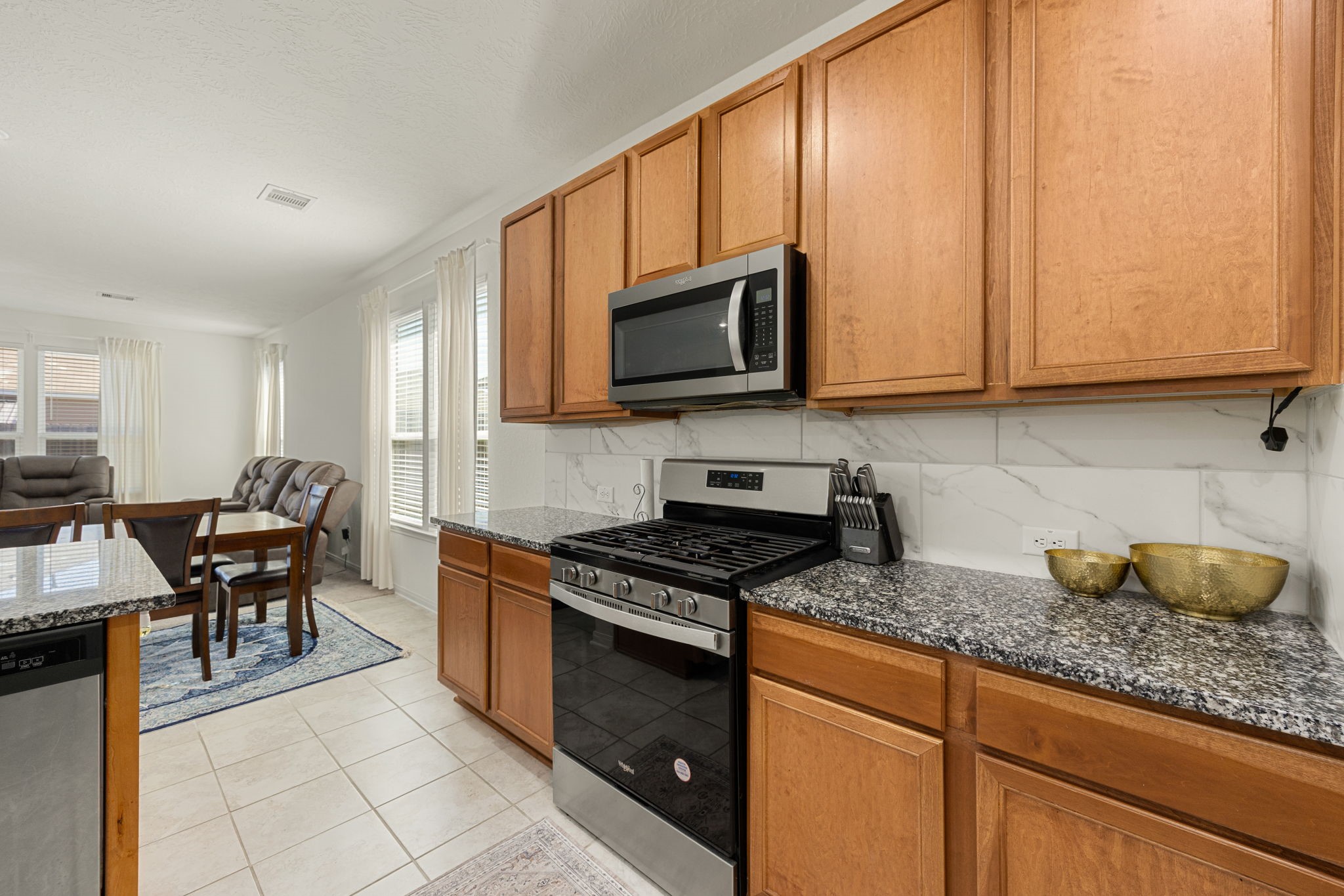 The beautifully appointed kitchen showcases a classic balance of warmth and modern design. Premium granite countertops are paired with a timeless marble-patterned tile backsplash, while matching stainless steel Whirlpool appliancesincluding a built-in microwave and gas rangecreate a highly functional workspace for any home chef.