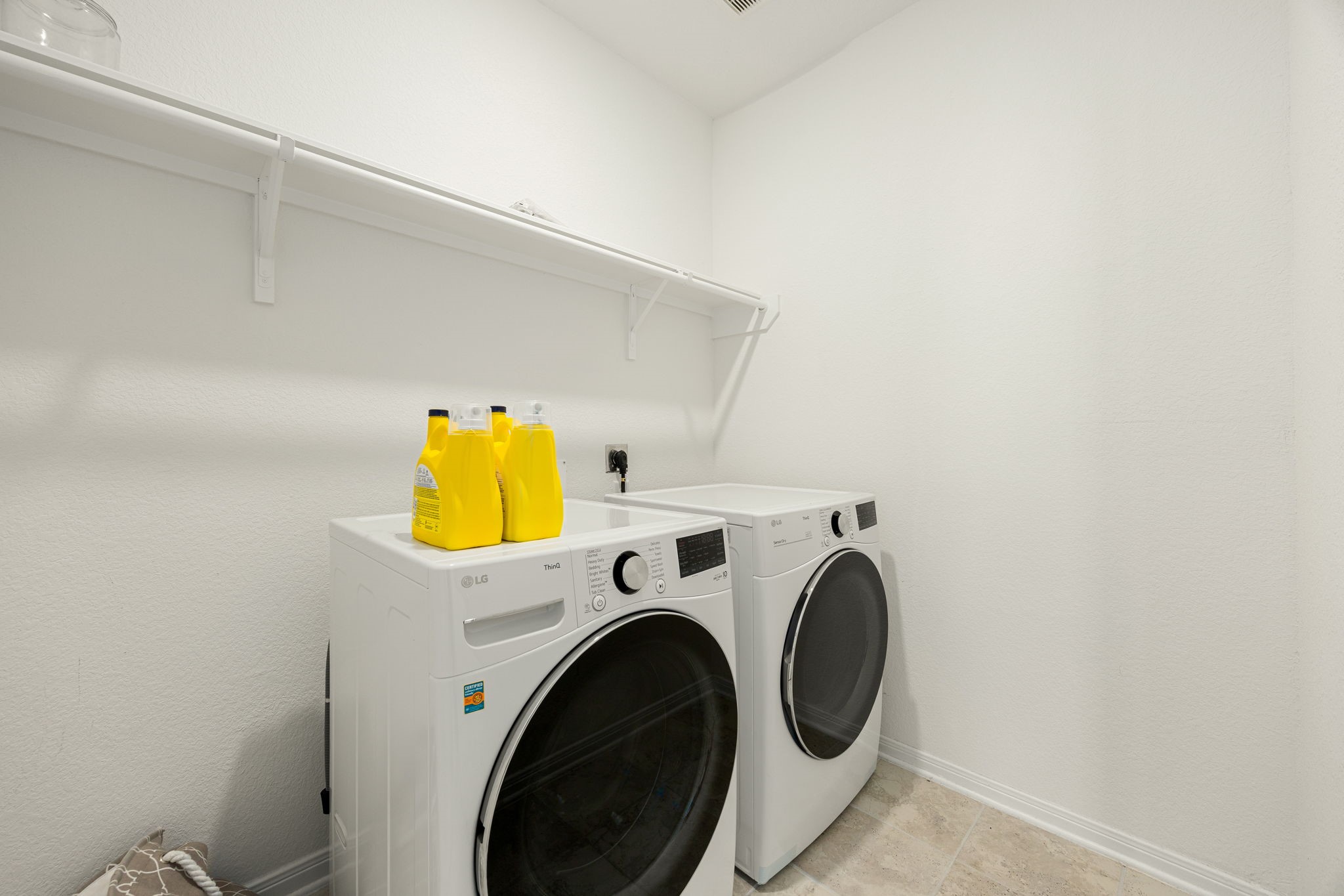 A beautifully clean and bright laundry zone located conveniently within the home's layout. Modern recessed lighting illuminates the space, which boasts premium tile flooring and extensive overhead shelving, offering the perfect blend of practical workspace and organized storage.