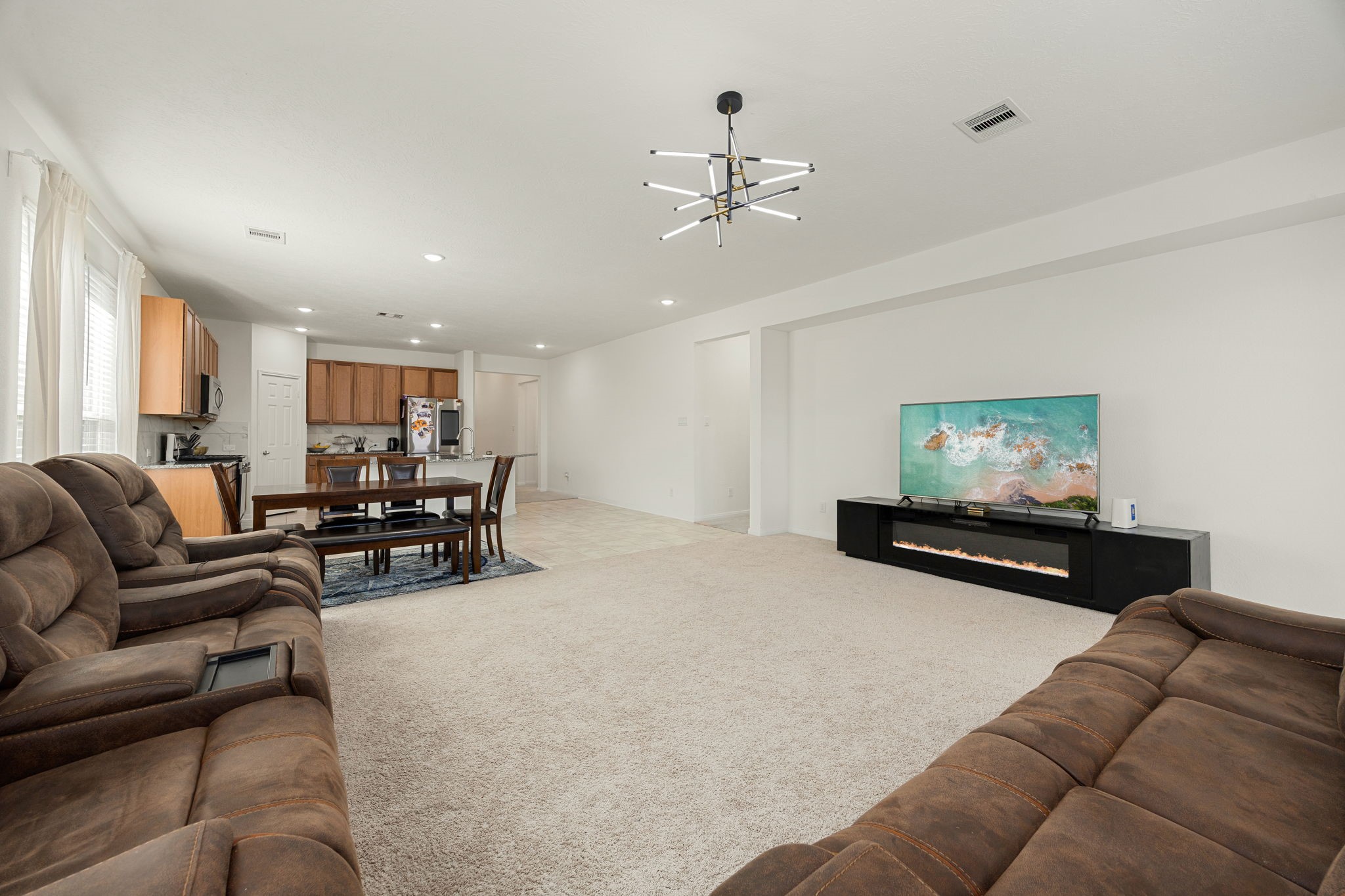 Anchoring the main family room is a striking, contemporary sputnik-style chandelier that adds a touch of modern sophistication to the home's high ceilings. This vantage point perfectly showcases the ultimate open-concept layout, demonstrating how smoothly the main seating area flows directly back into the casual dining zone and kitchen hub for cohesive daily living.