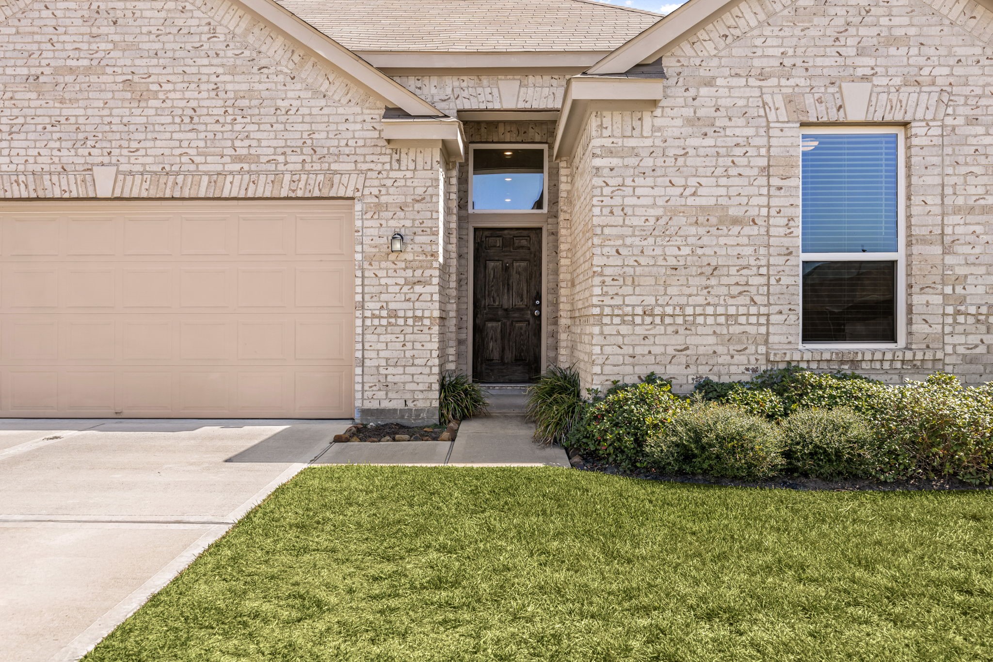 This beautifully maintained brick home features a spacious two-car garage, a manicured front lawn, and an inviting covered entryway that opens up into a bright, welcoming interior.