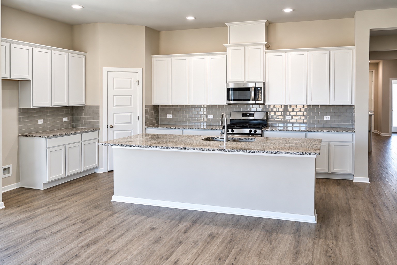Spacious kitchen featuring a large work island with seating, granite countertops, white cabinetry, stainless steel appliances, and a tile backsplash. Generous counter space and abundant storage make meal preparation and entertaining a breeze.