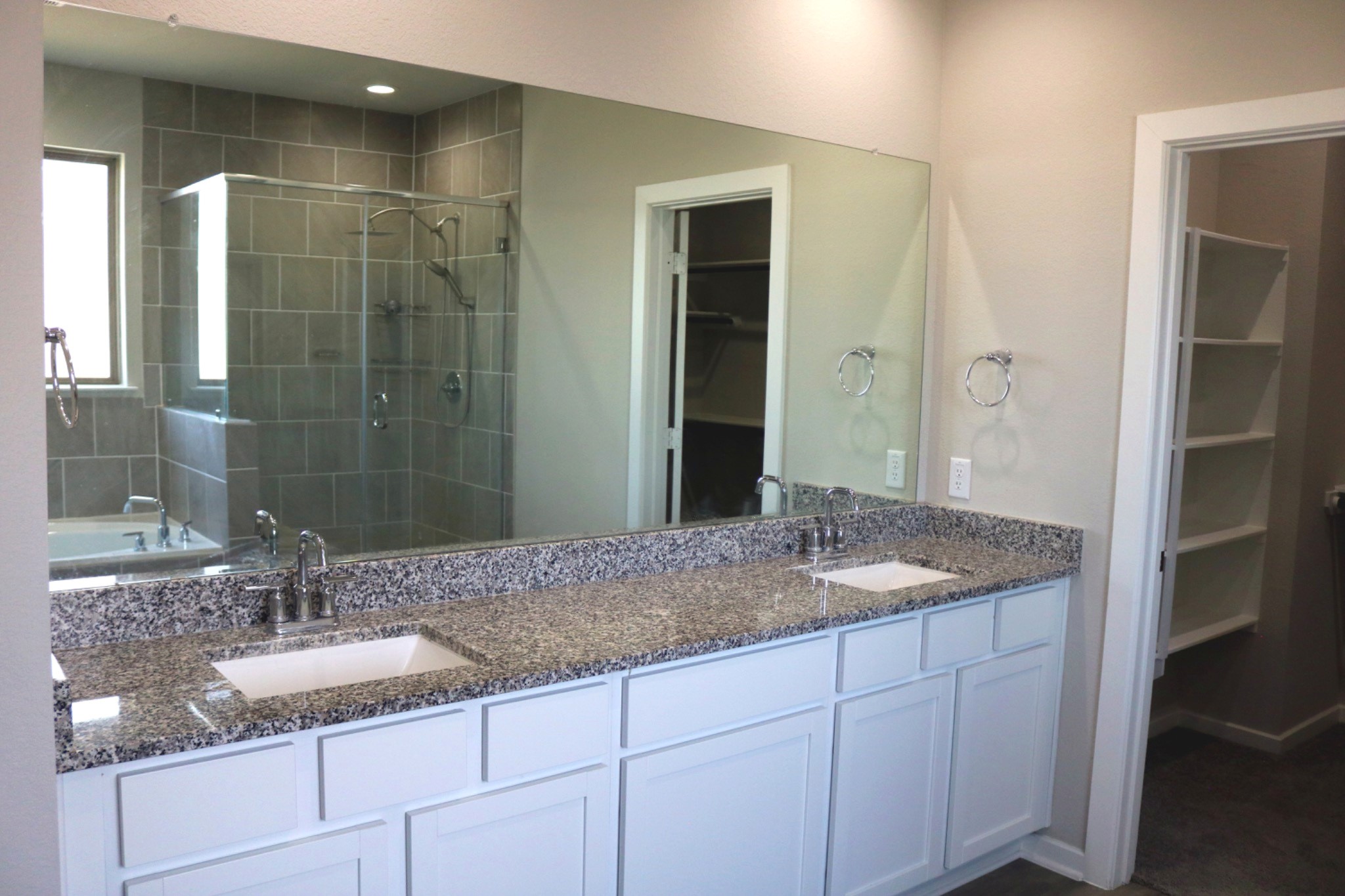 Primary bath featuring two separate vanities with granite countertops, generous cabinet storage, and a large mirror, providing plenty of space for everyday routines.