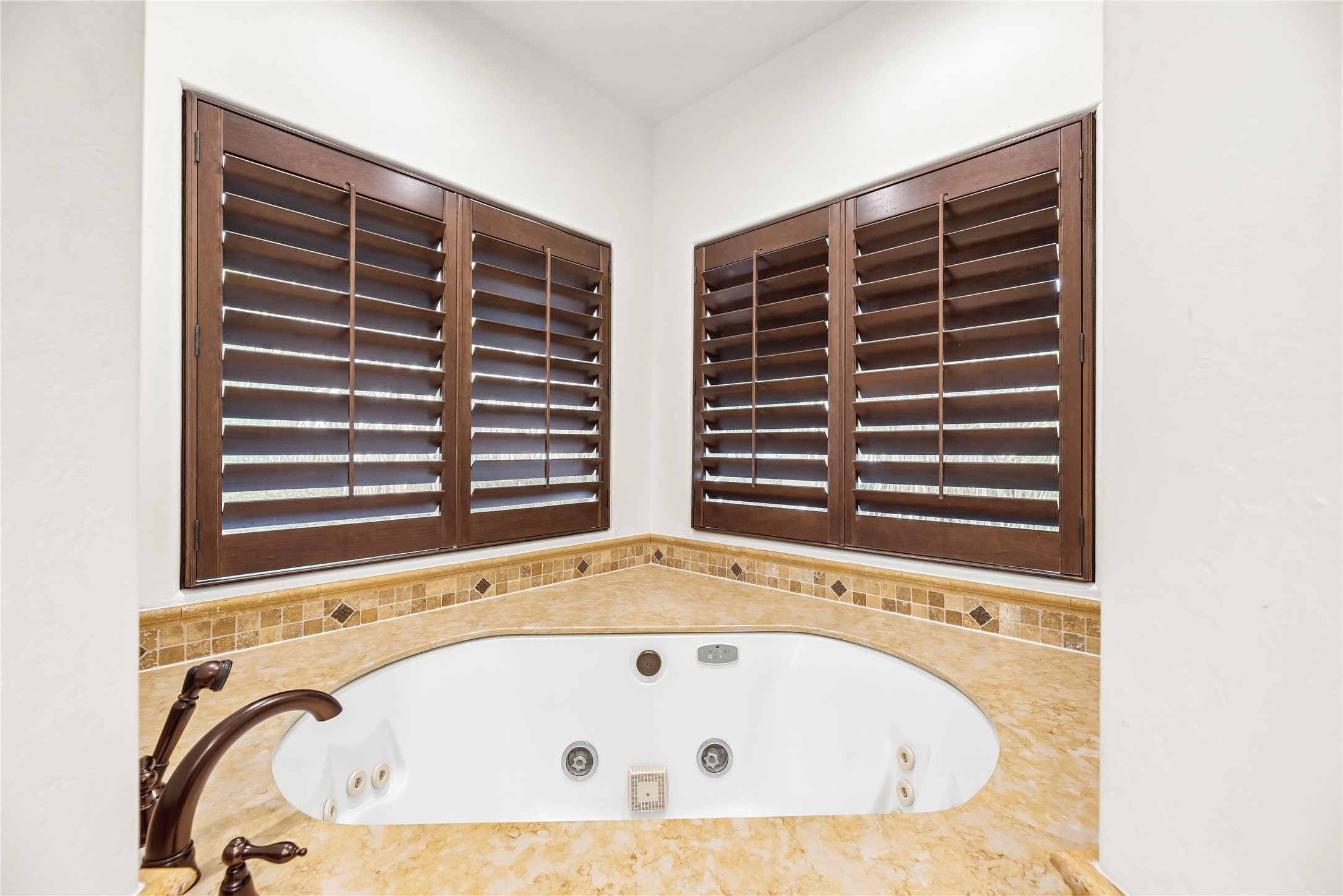 A deep jetted tub is framed by elegant tile work and large windows, creating a peaceful corner to unwind after a long day.