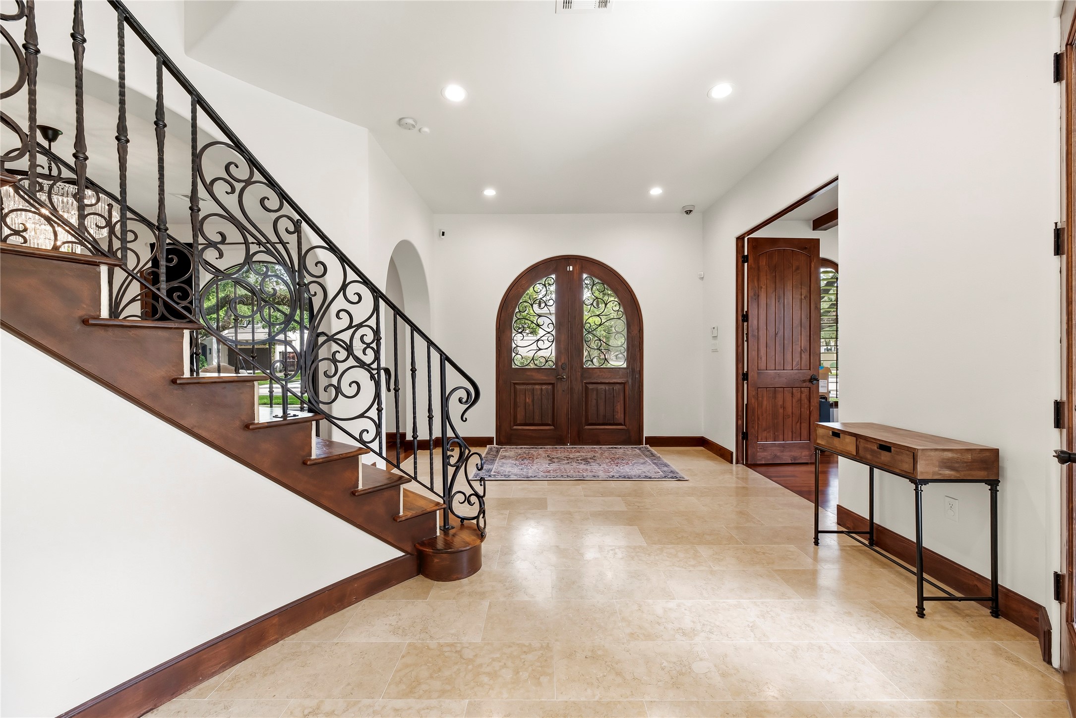 Stunning arched wood double doors open to a soaring foyer featuring travertine flooring and a custom wrought-iron staircase, setting a tone of timeless luxury from the moment you arrive.