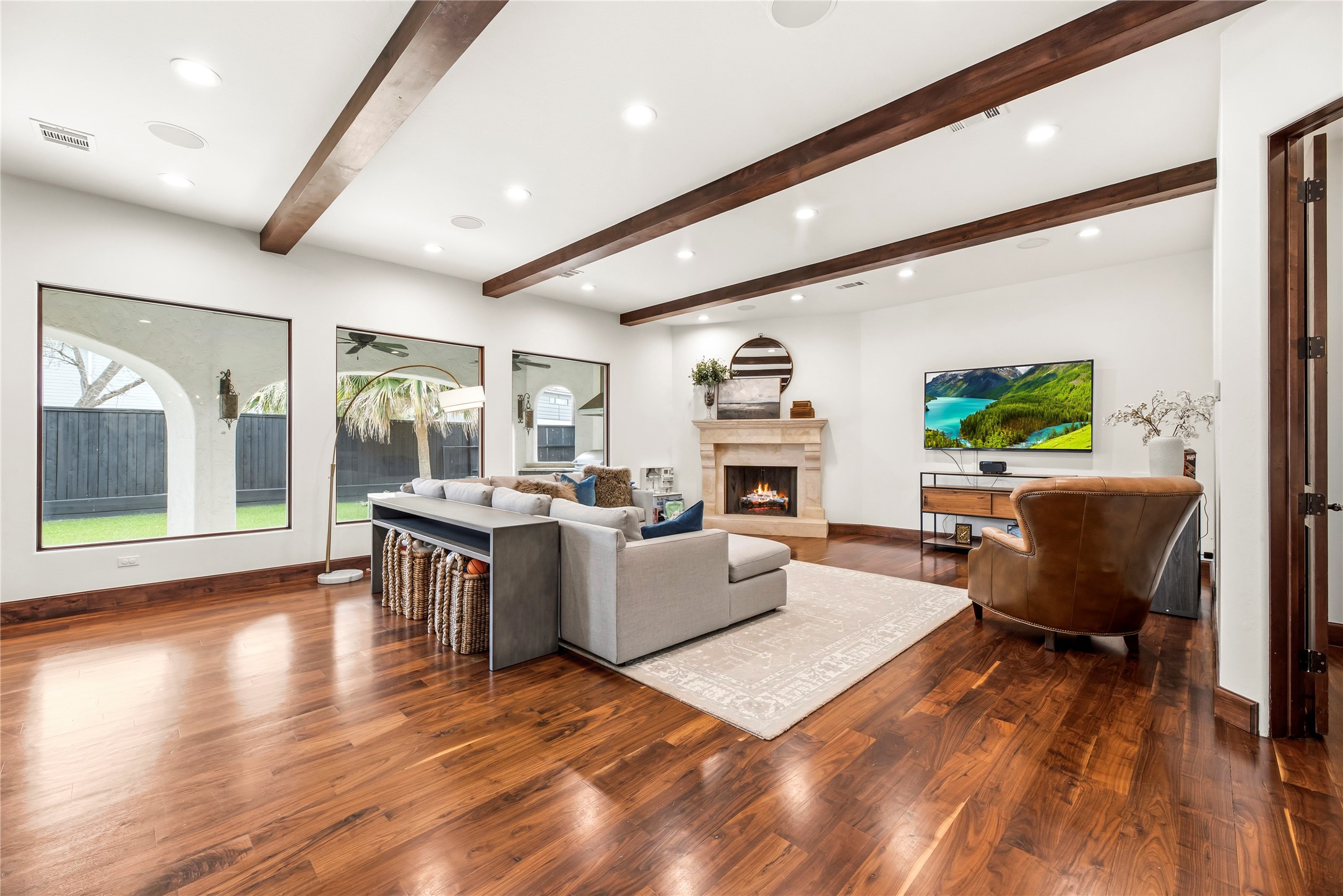 This luxurious living area is anchored by custom ceiling beams and a stately gas fireplace. Large windows frame peaceful views of the private grounds, creating a sophisticated retreat that blends architectural elegance with a serene outdoor backdrop.