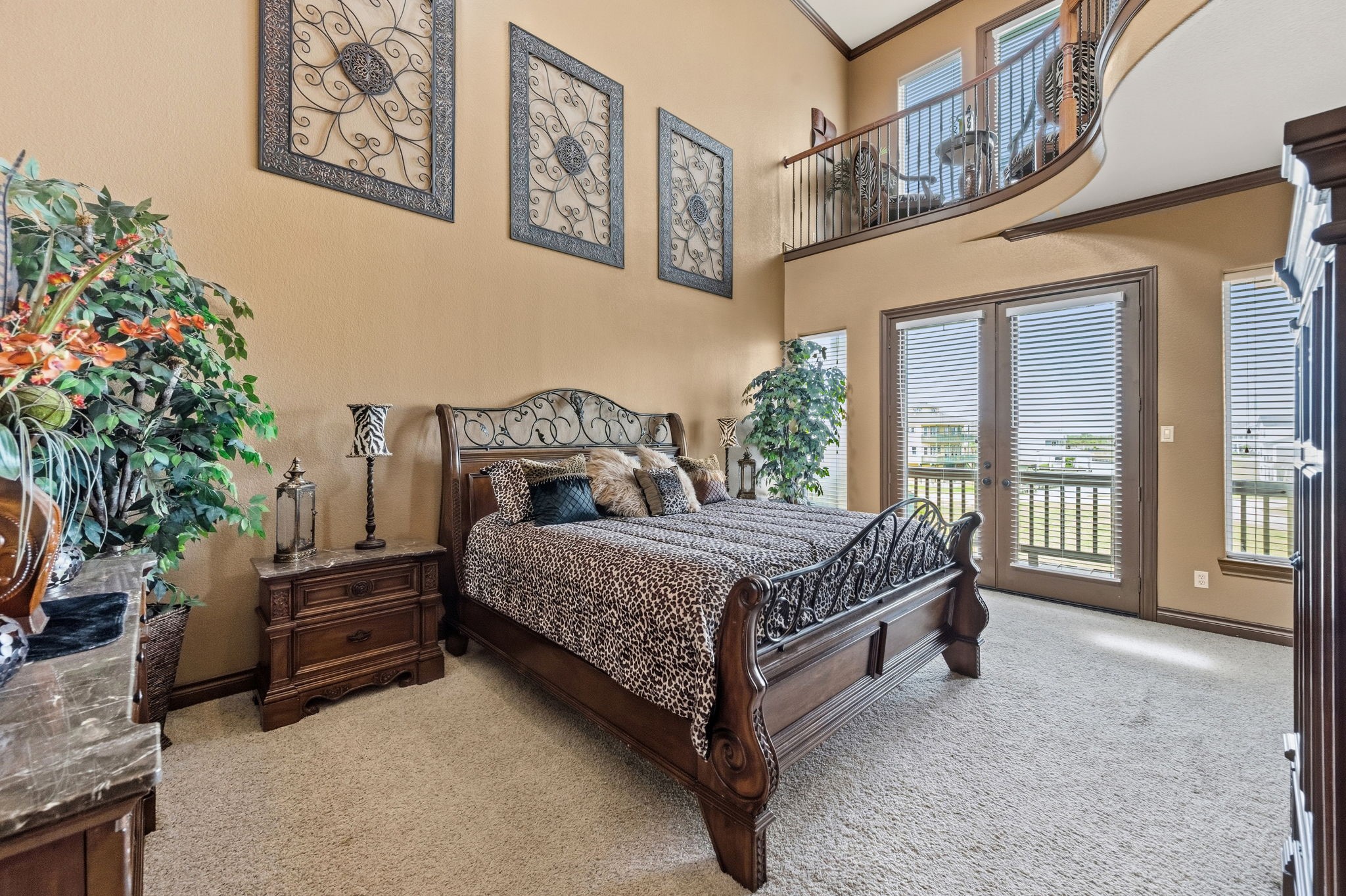 Spacious primary bedroom with high ceilings and elegant decor, featuring a luxurious bed, large windows for natural light, and a charming loft area above.
