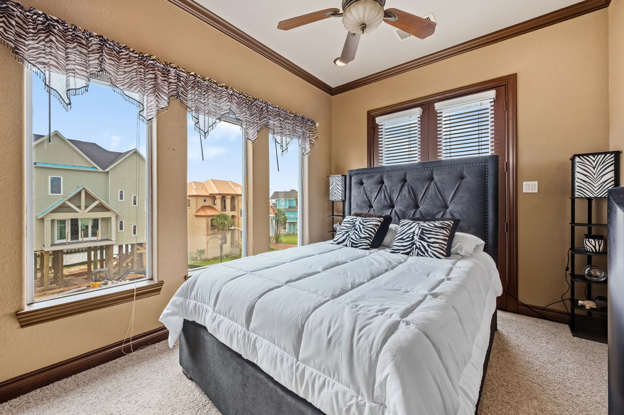 3rd bedroom with large windows offering scenic views, featuring a plush bed with stylish zebra print accents and a ceiling fan for added comfort.
