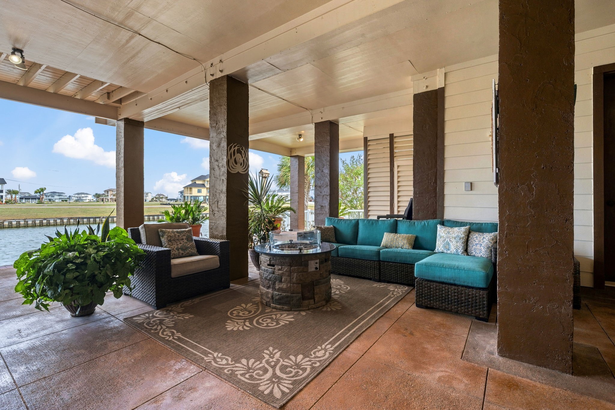 Stylish covered patio with cozy seating, lush plants, and a tranquil water view, perfect for relaxing or entertaining.