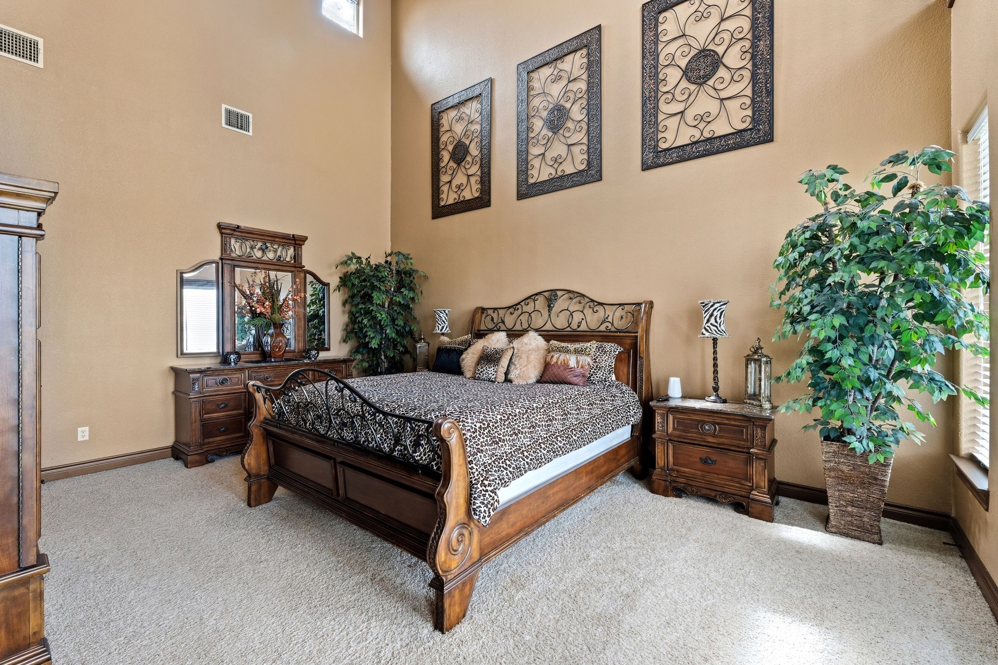 Elegant primary bedroom featuring a high ceiling, rich wooden furniture, and large windows that fill the space with natural light.
