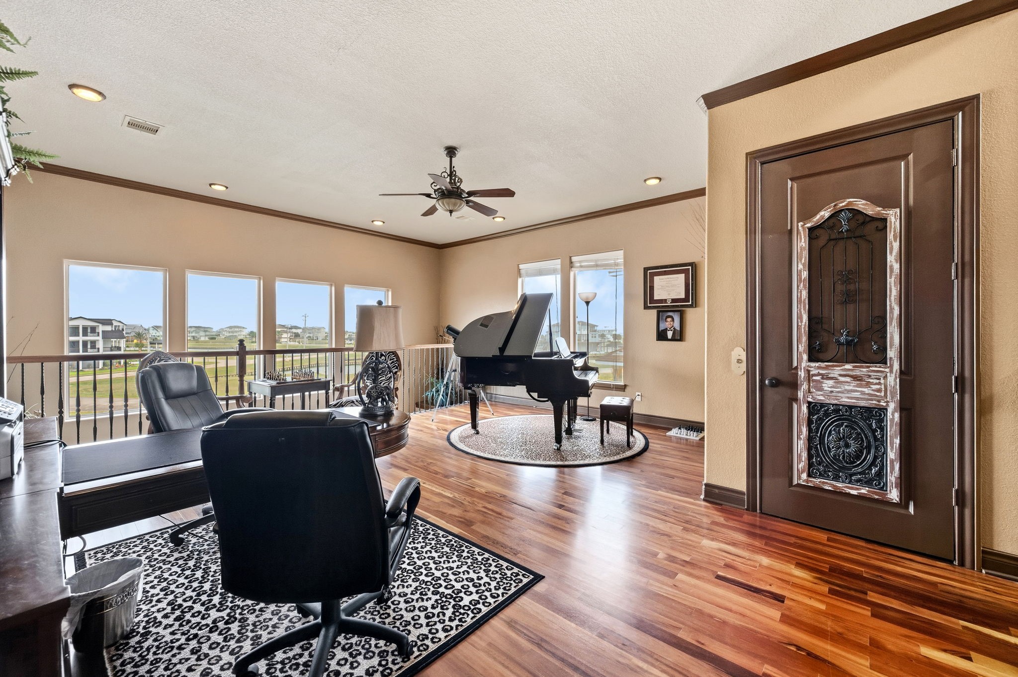 Spacious and elegant home office featuring rich wood flooring, abundant natural light from large windows, and a sophisticated ambiance highlighted by a grand piano.