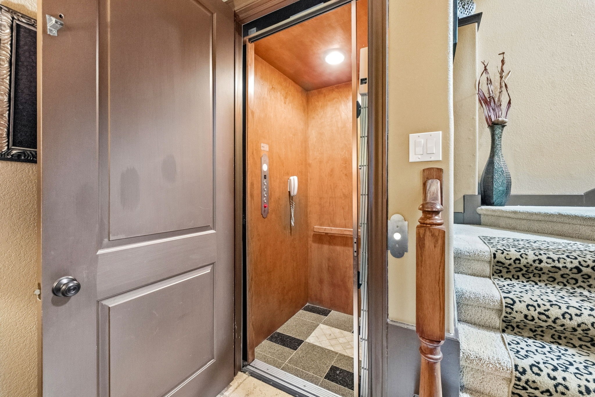 Elegant home featuring a convenient in-house elevator adjacent to a stylish staircase with leopard print carpeting.