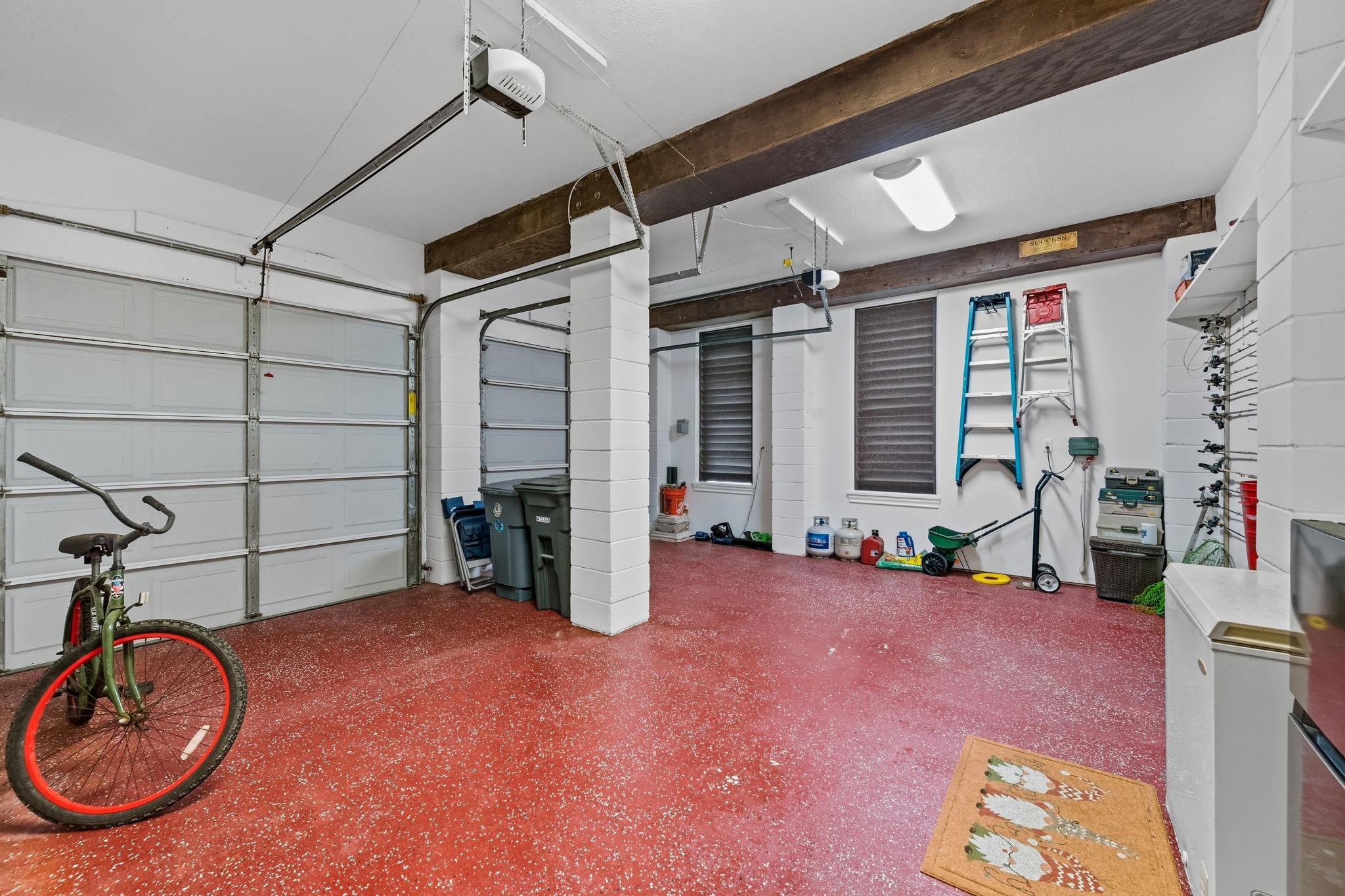 Spacious two-car garage with durable red flooring, ample storage space, and convenient shelving, perfect for organizing tools and outdoor equipment.