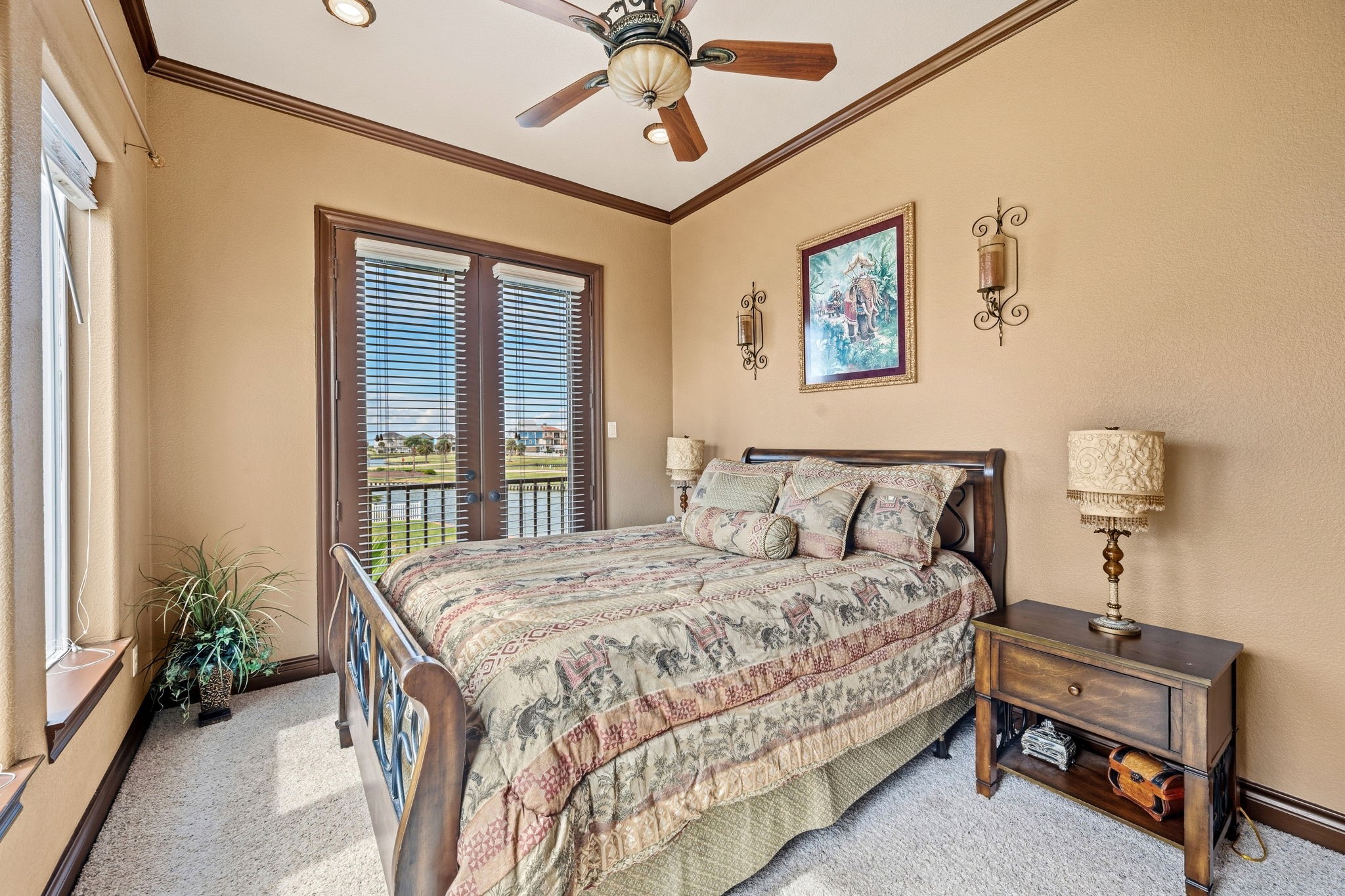 1st floor bedroom featuring warm earth tones, a stylish ceiling fan, and abundant natural light through French doors with scenic views.