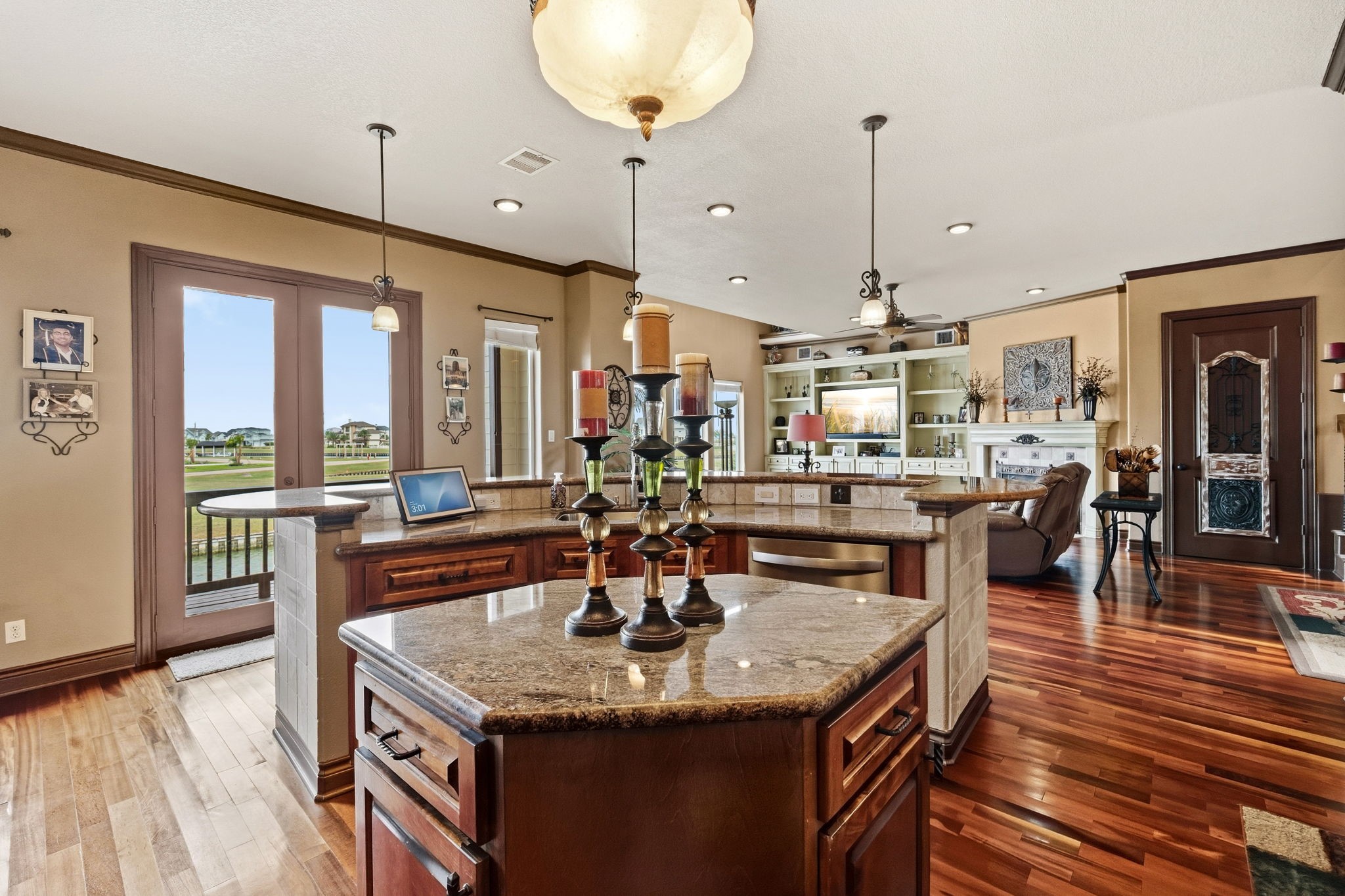 Spacious open-concept living area featuring elegant hardwood floors, a large kitchen island with granite countertops, and ample natural light from expansive windows overlooking a serene view.