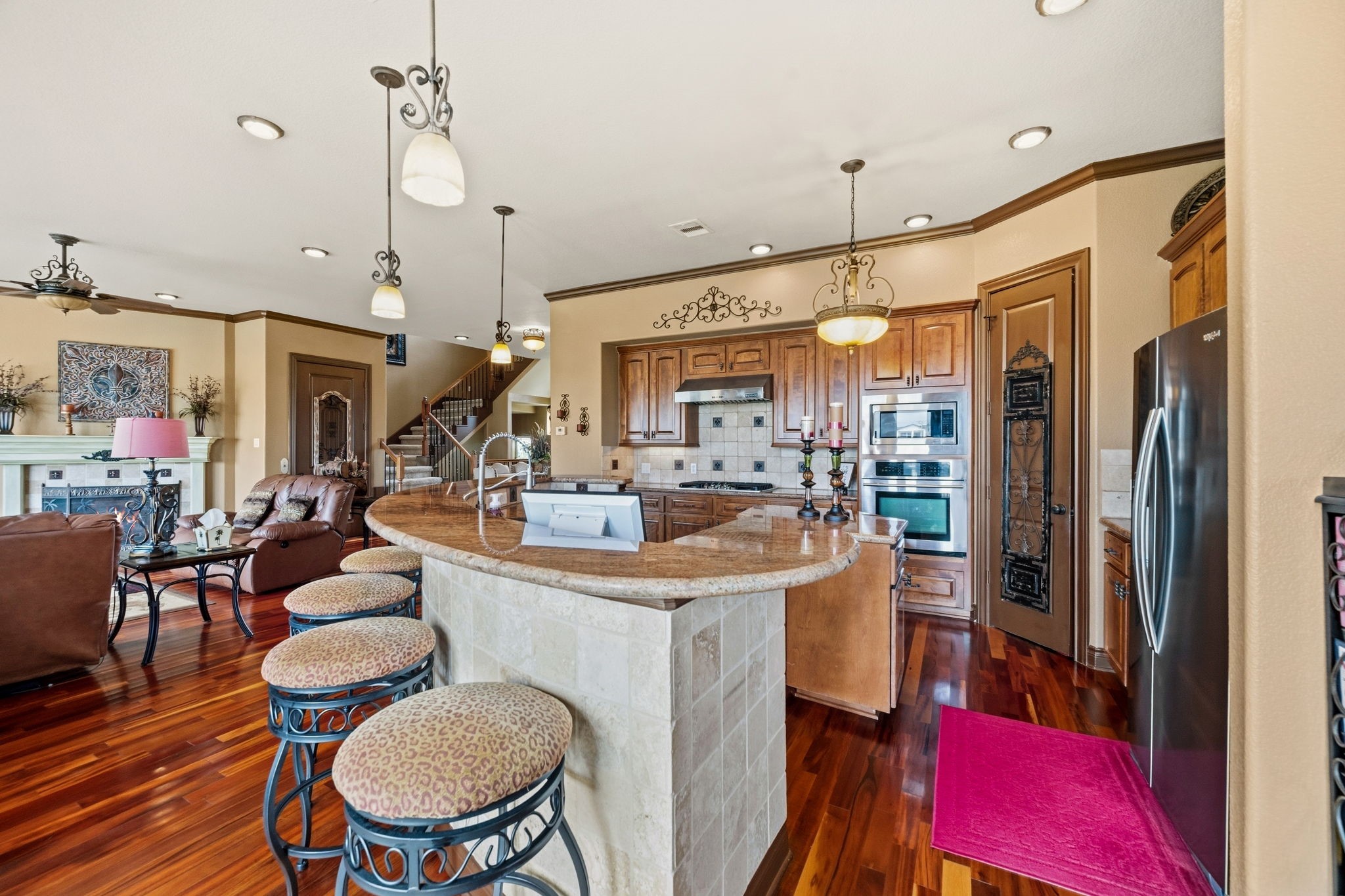 Elegant open-concept kitchen and living area featuring rich hardwood floors, a curved breakfast bar with stylish stools, and custom wood cabinetry.