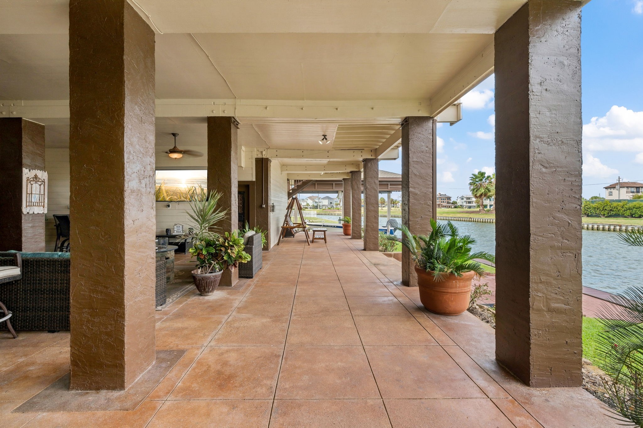 Expansive covered patio with elegant columns and lush potted plants, offering stunning waterfront views and ample space for outdoor relaxation and entertainment.