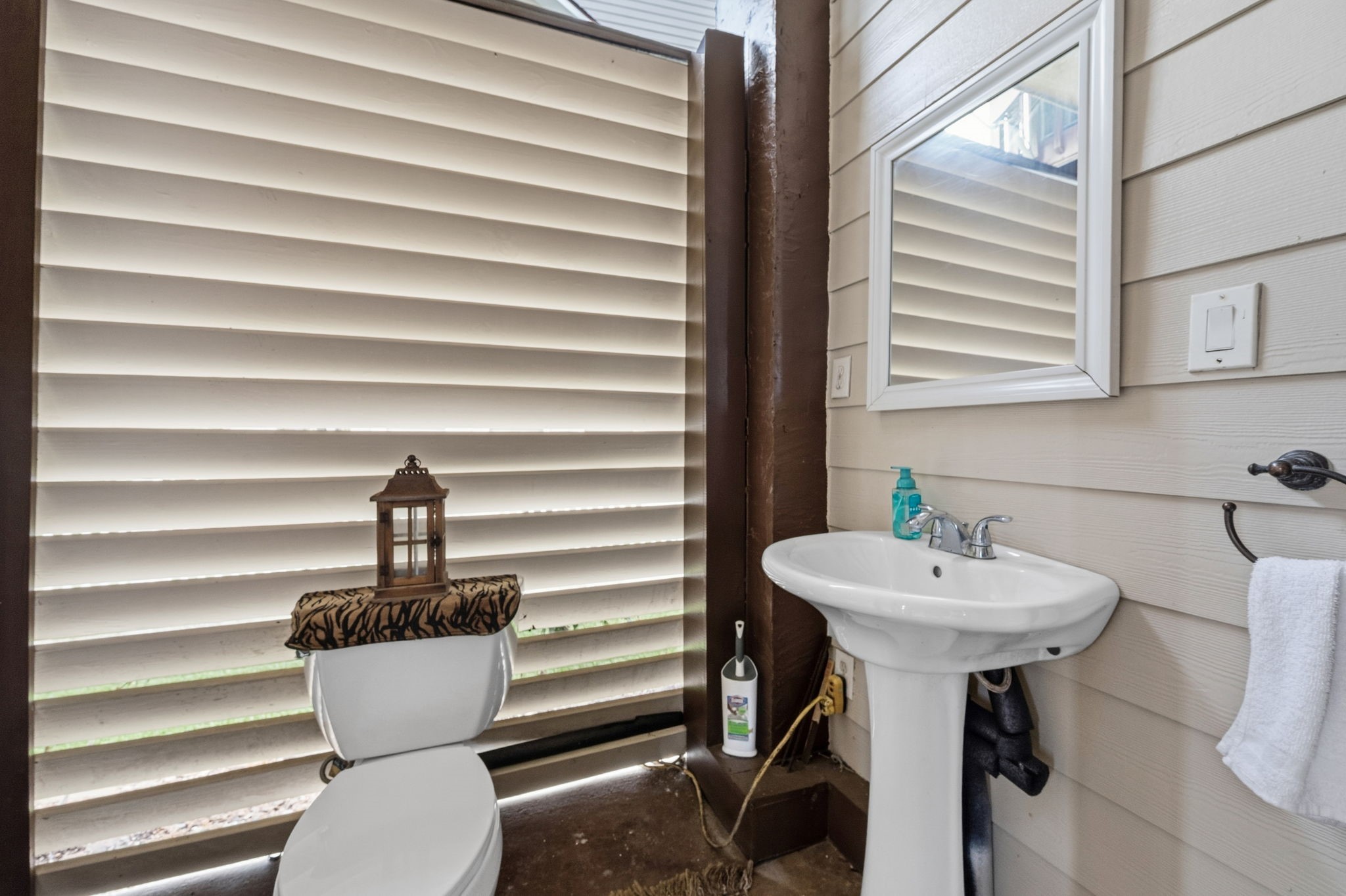Charming outdoor bathroom with privacy shutters, featuring a pedestal sink and stylish accents.