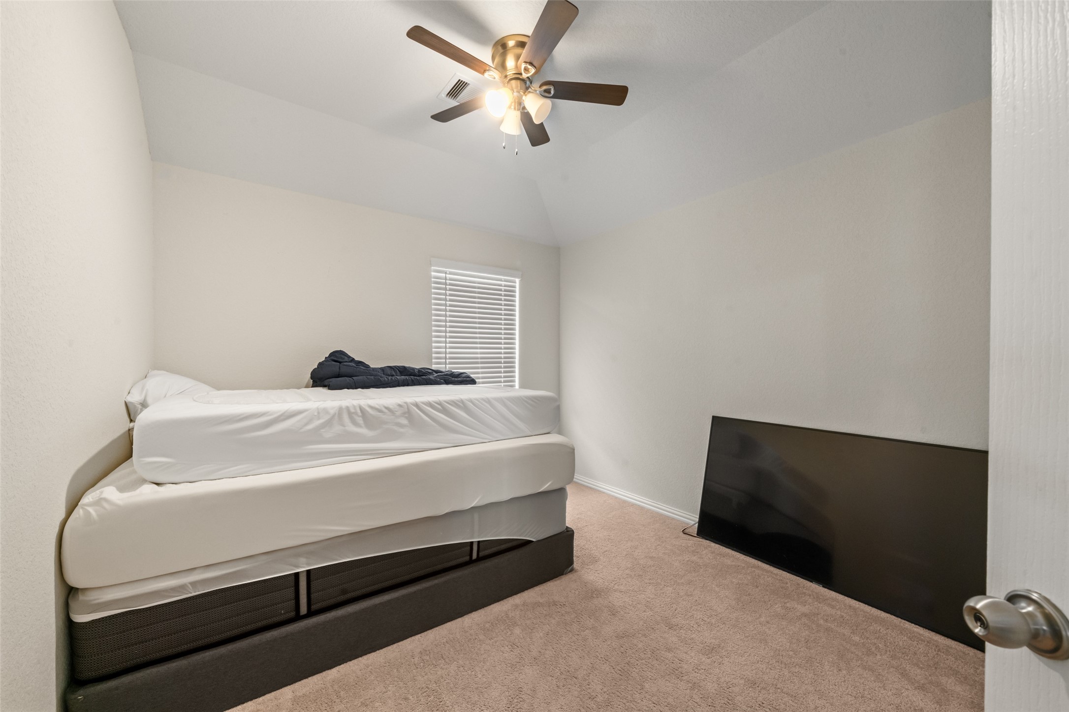 Cozy bedroom featuring plush carpeting, a ceiling fan, and ample natural light from a well-sized window.