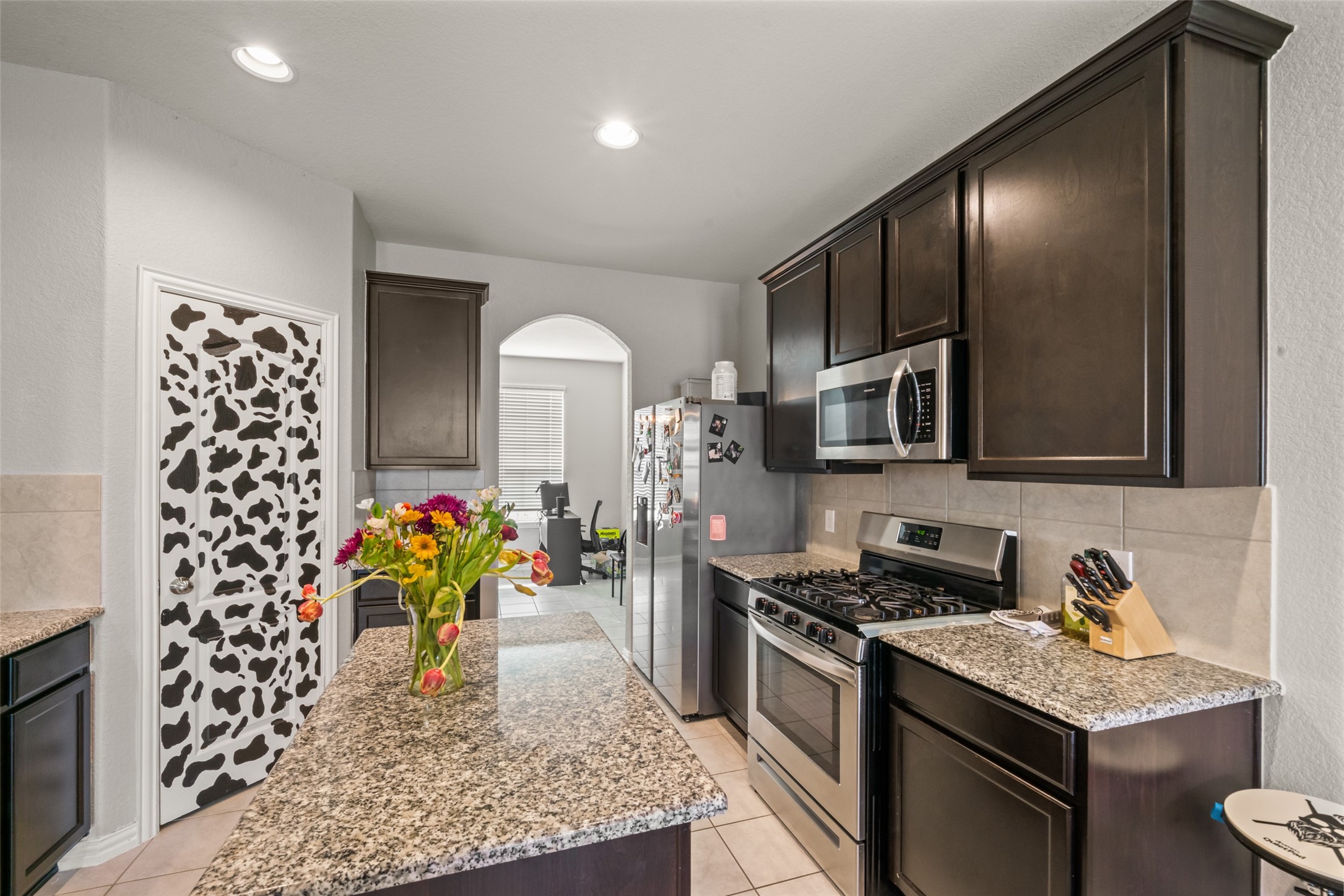 Modern kitchen with sleek dark cabinetry, granite countertops, and stainless steel appliances. A unique cow-print pantry door adds a fun touch, while a central island provides extra workspace.