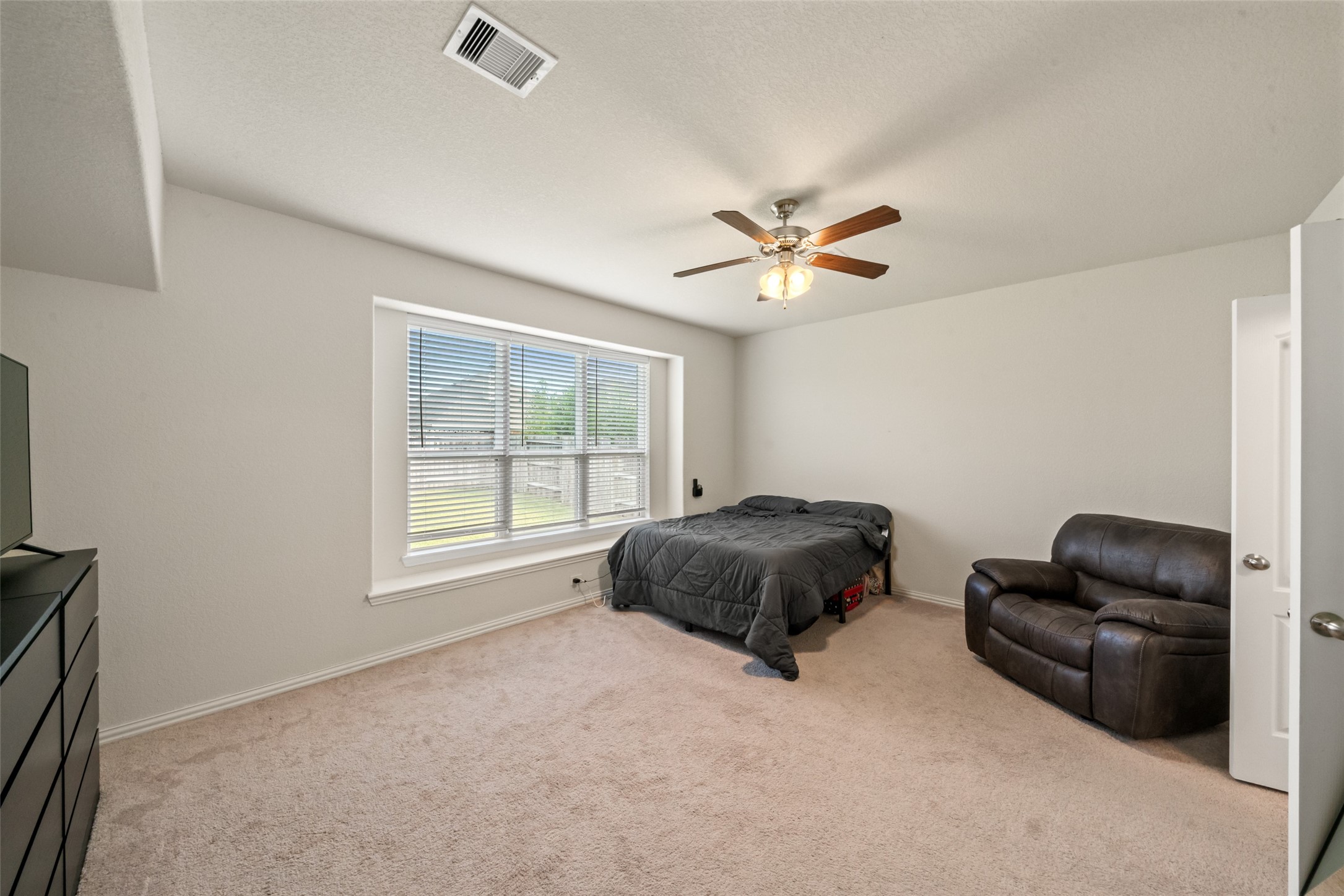 Spacious bedroom with abundant natural light, featuring a large window, ceiling fan, and cozy carpet flooring.
