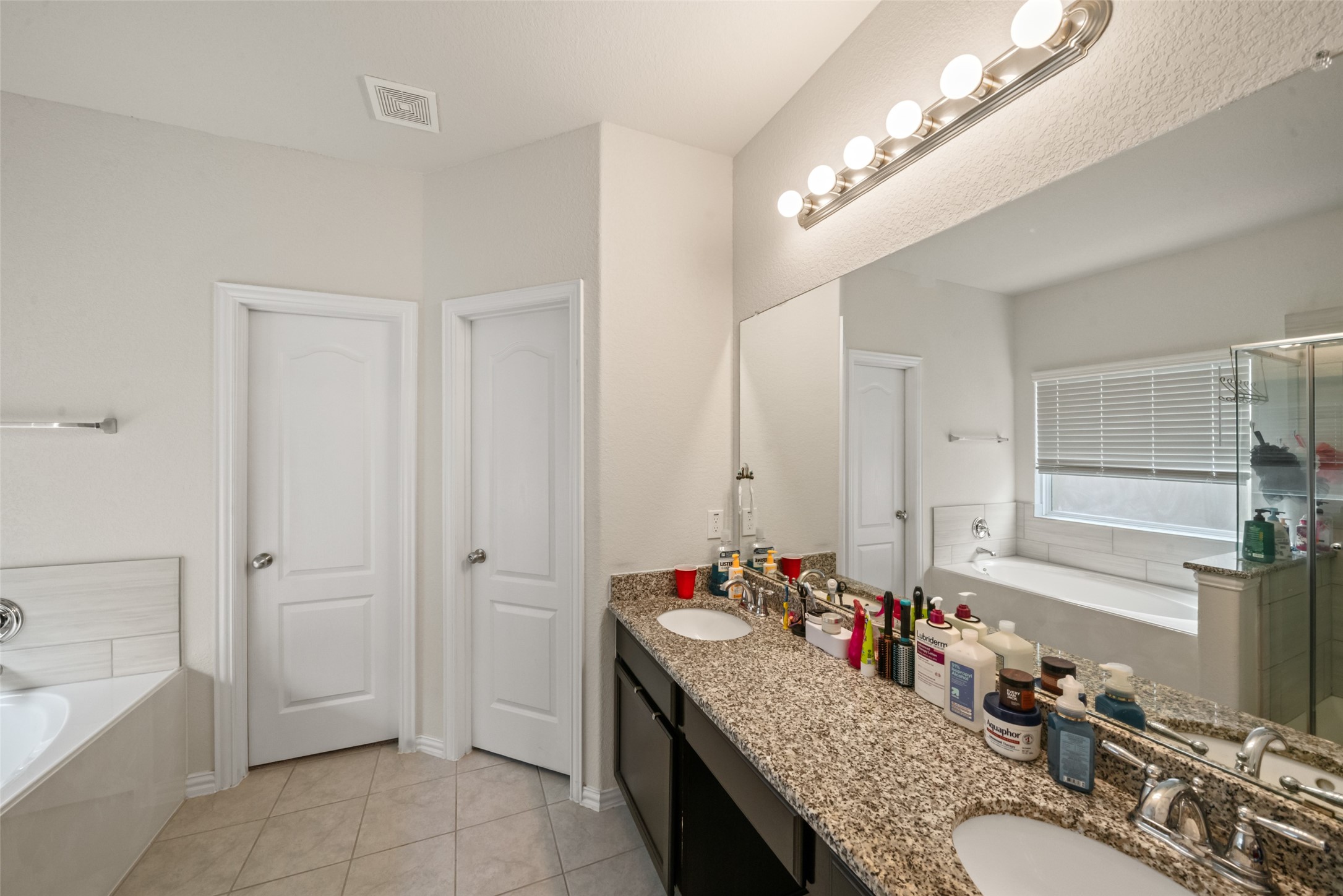 Elegant bathroom featuring a granite double vanity, ample mirror space, and a luxurious soaking tub with natural light streaming in.