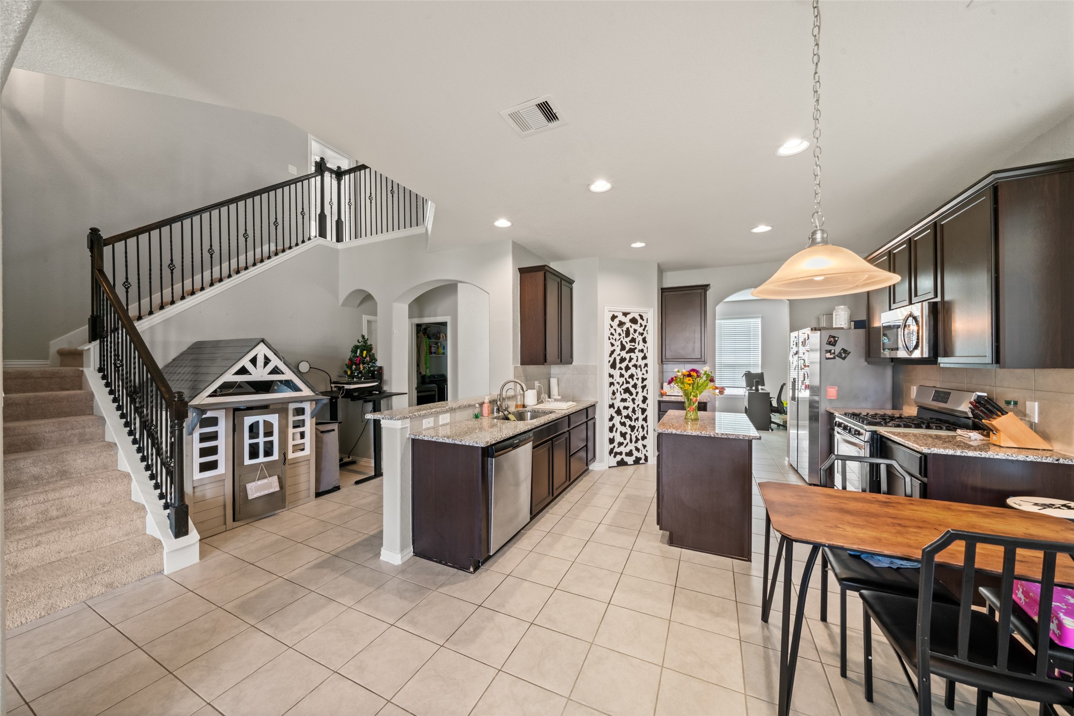 Spacious kitchen with sleek dark cabinetry, granite countertops, and modern appliances, complemented by an adjacent cozy dining area and stylish staircase.