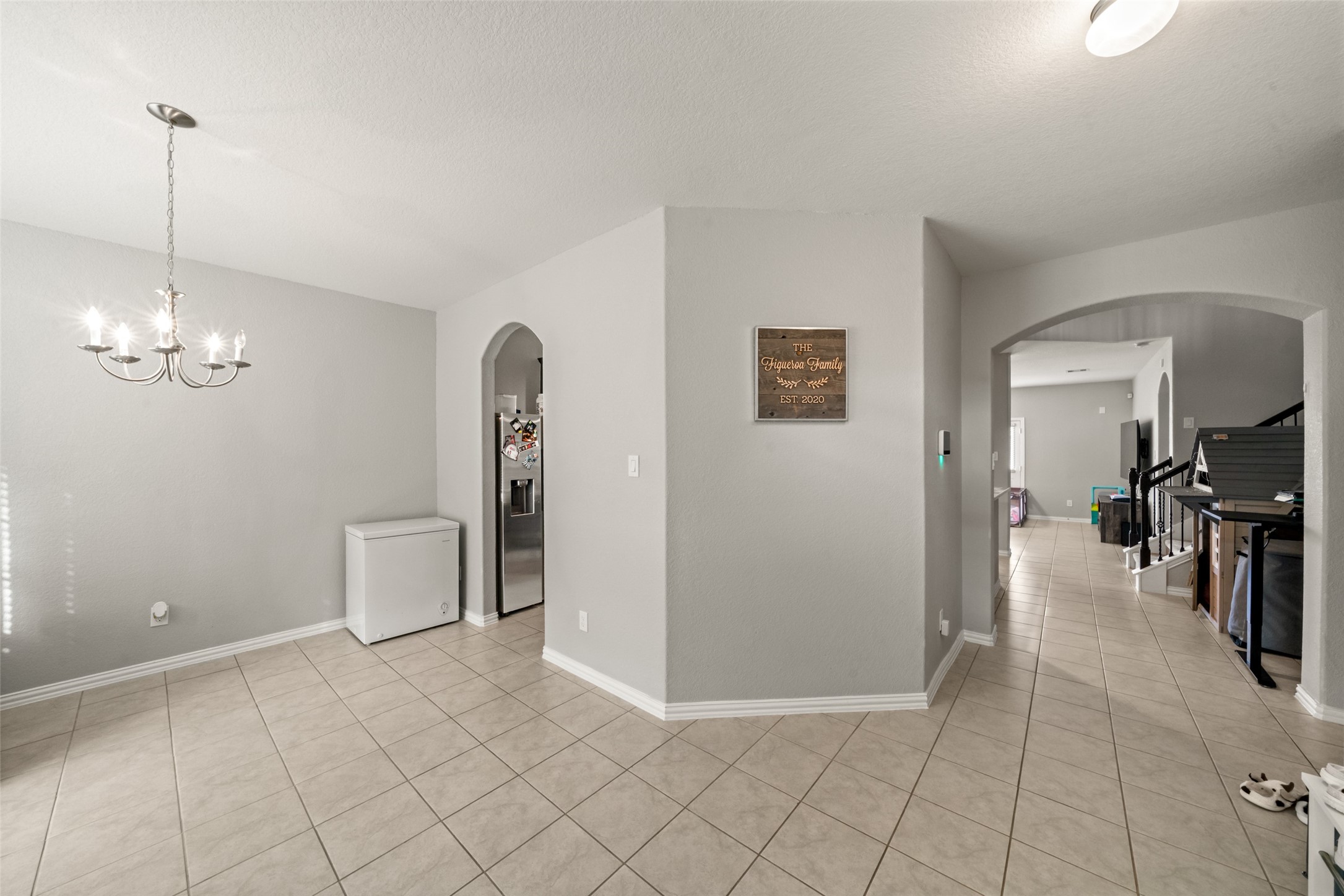 Bright and spacious dining area with elegant chandelier lighting, tile flooring, and convenient access to the kitchen and living spaces through arched doorways.