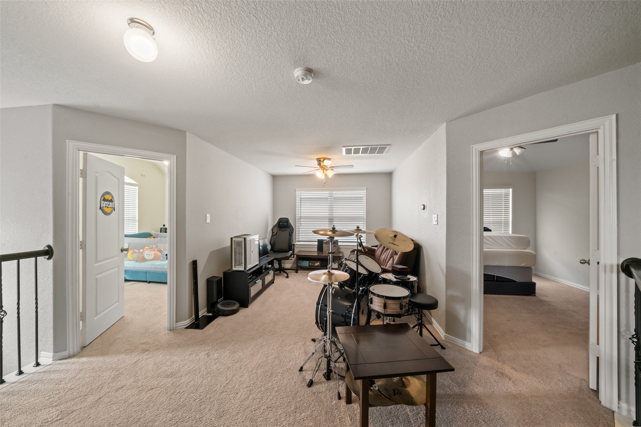 Spacious upstairs bonus room with versatile potential, featuring a cozy carpeted area perfect for a music setup or gaming zone, flanked by two bedrooms with ample natural light.