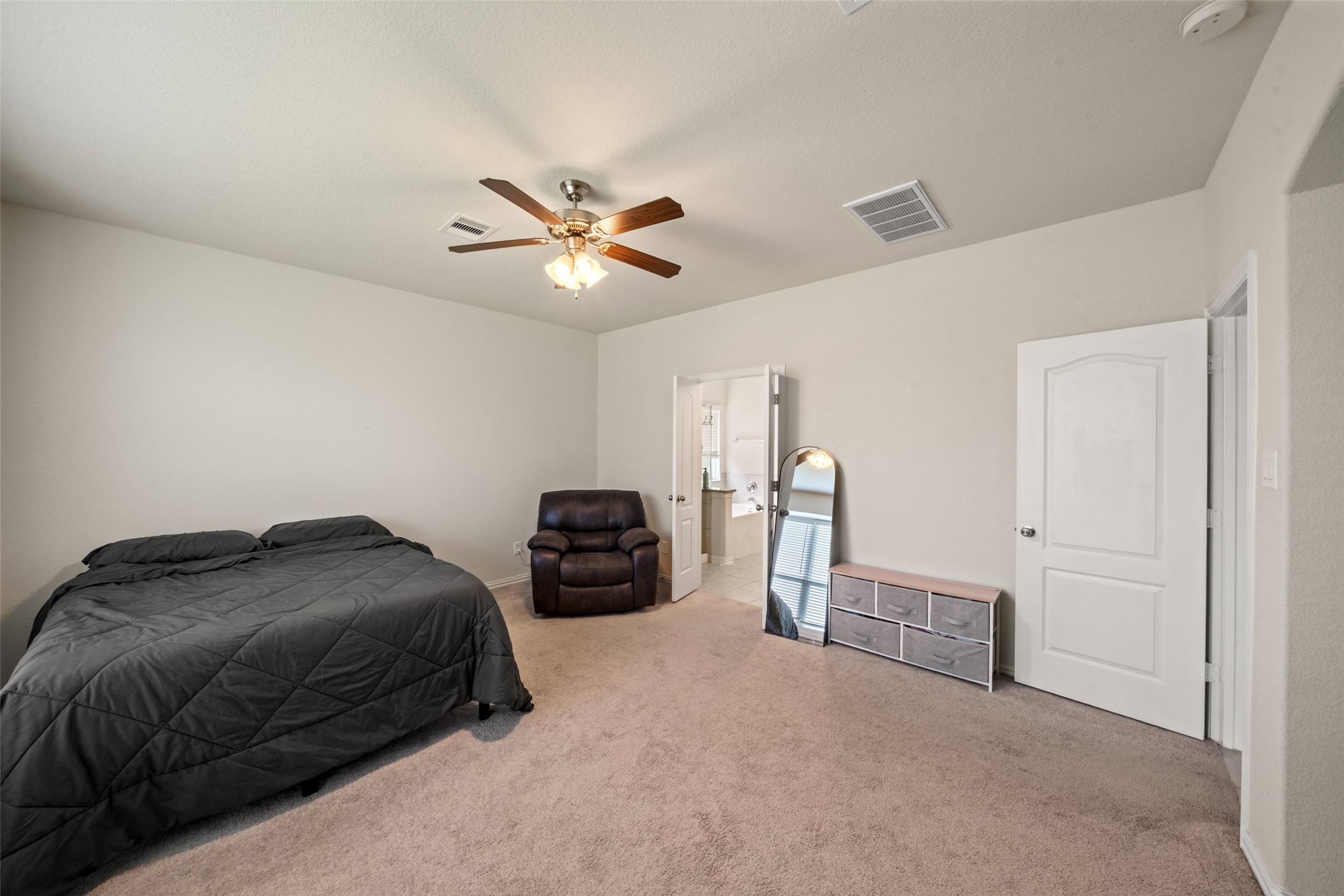 Spacious bedroom featuring plush carpeting, a ceiling fan, and an en-suite bathroom for added convenience.