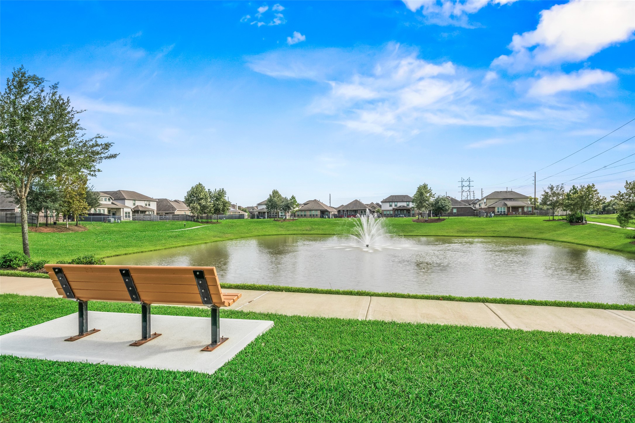 Enjoy serene views of the community pond with a charming fountain, perfect for relaxation on the nearby bench amidst lush greenery.