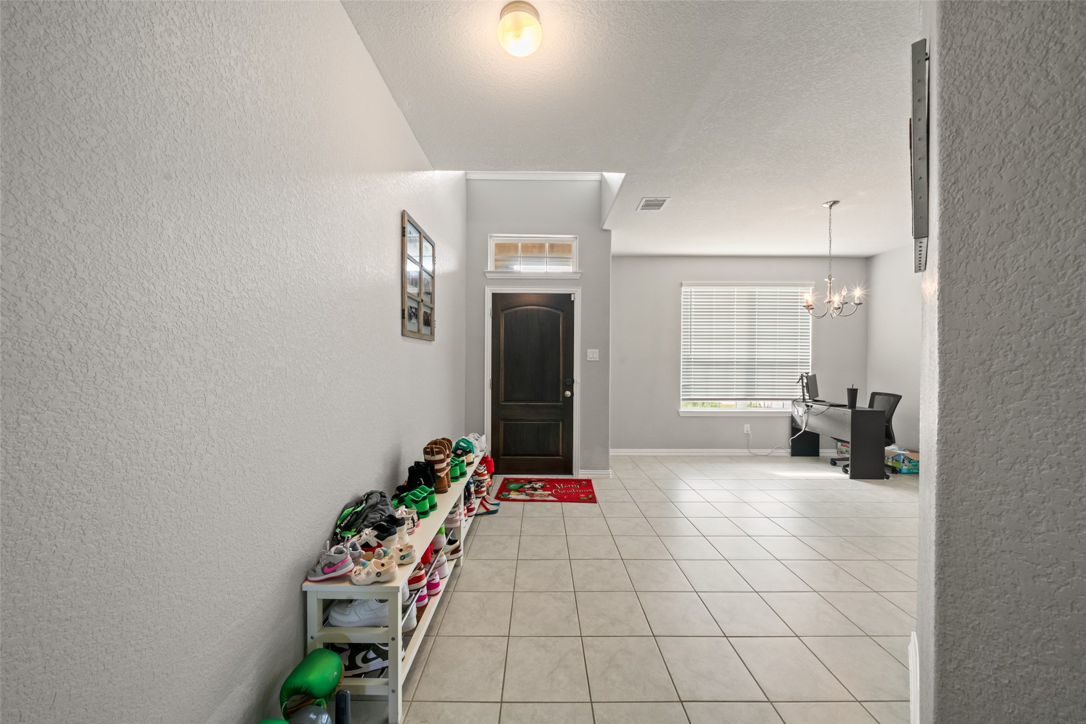 Bright and welcoming entryway with tiled flooring, leading to a spacious room perfect for an office or additional living space, enhanced by a large window.