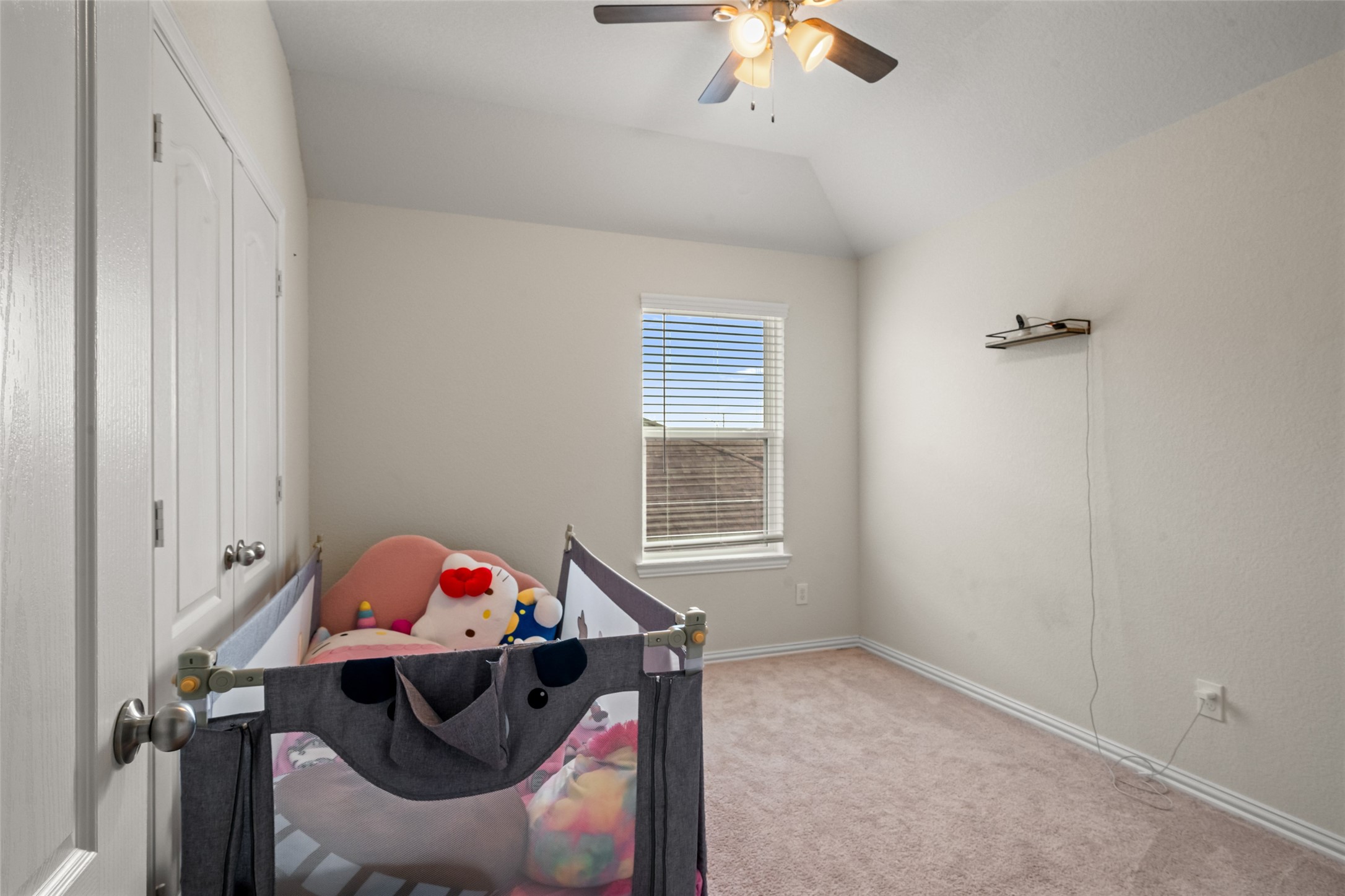 Cozy nursery with soft carpeting, a ceiling fan, and natural light from a large window, offering a serene space for your little one.