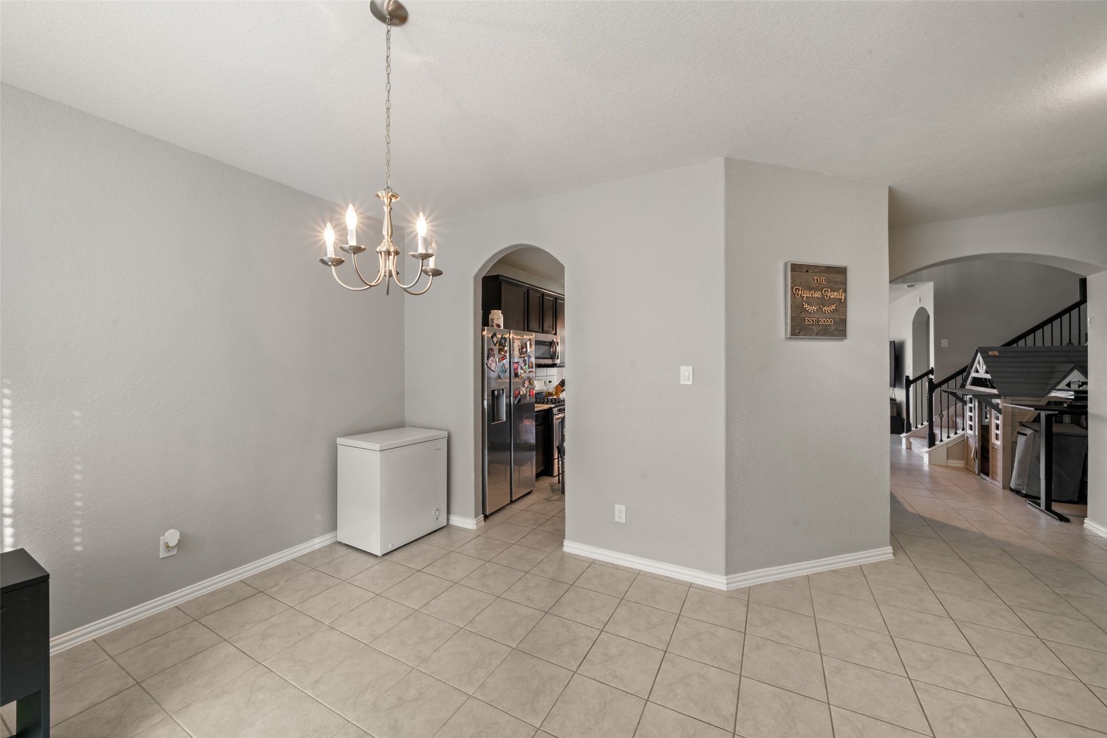 Bright and open dining area with elegant tile flooring, a charming chandelier, and convenient access to the kitchen and living spaces through stylish archways.