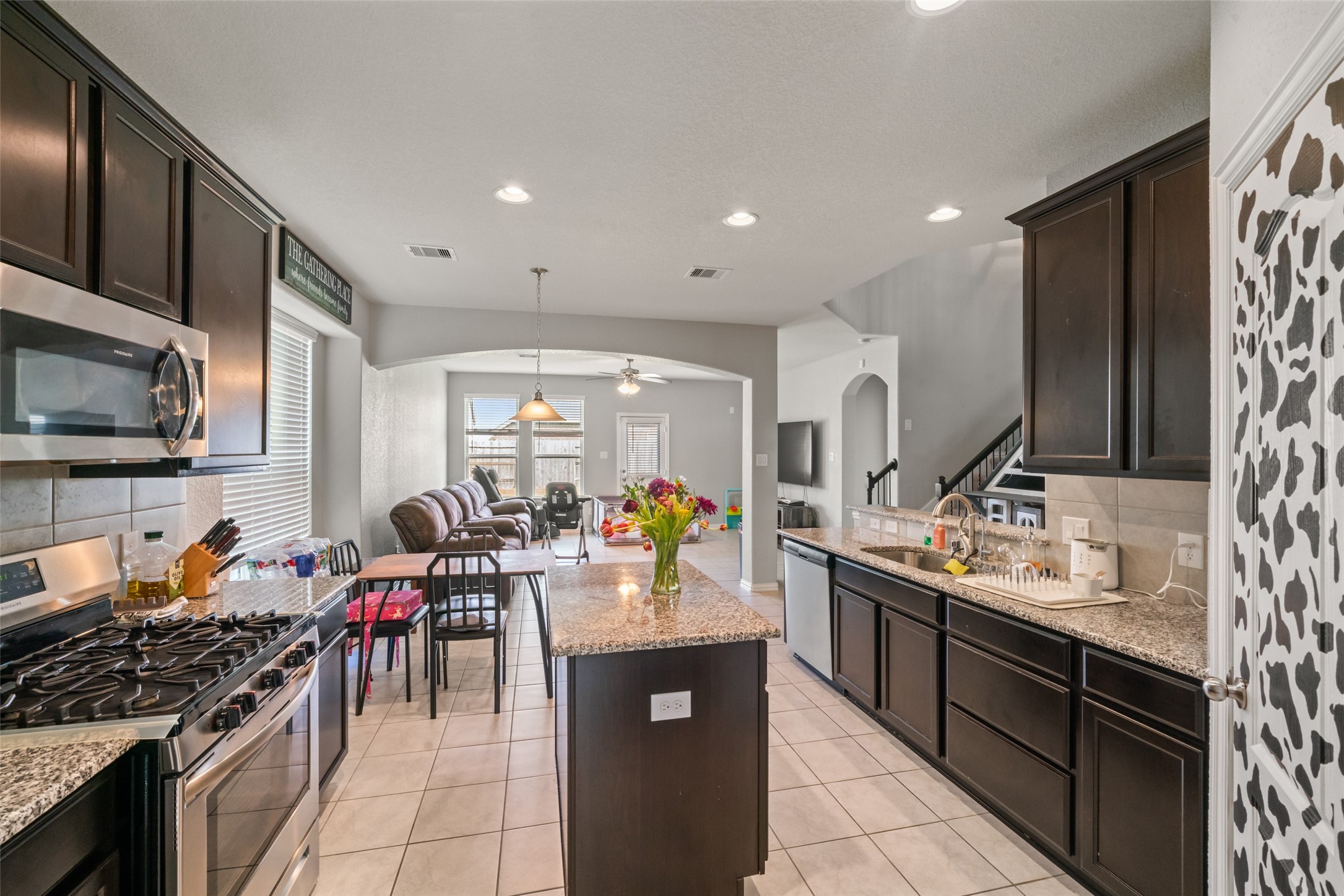 Spacious open-concept kitchen with dark cabinetry, granite countertops, and a central island, seamlessly flowing into a cozy living area with ample natural light. Spacious open-concept kitchen with dark cabinetry, granite countertops, and a central island, seamlessly flowing into a cozy living area with ample natural light.