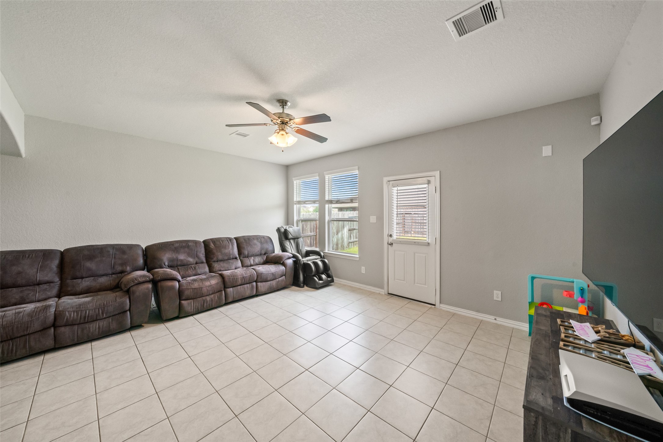 Spacious living area with tiled floors, ample natural light from large windows, and a area large enough to enjoy the game, perfect for relaxation and entertainment.