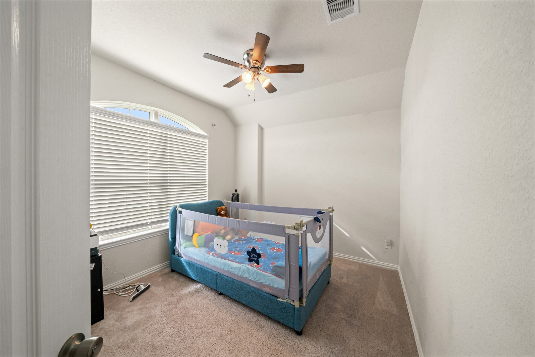 Cozy bedroom with soft carpeting, abundant natural light from a large window, and a ceiling fan for comfort.