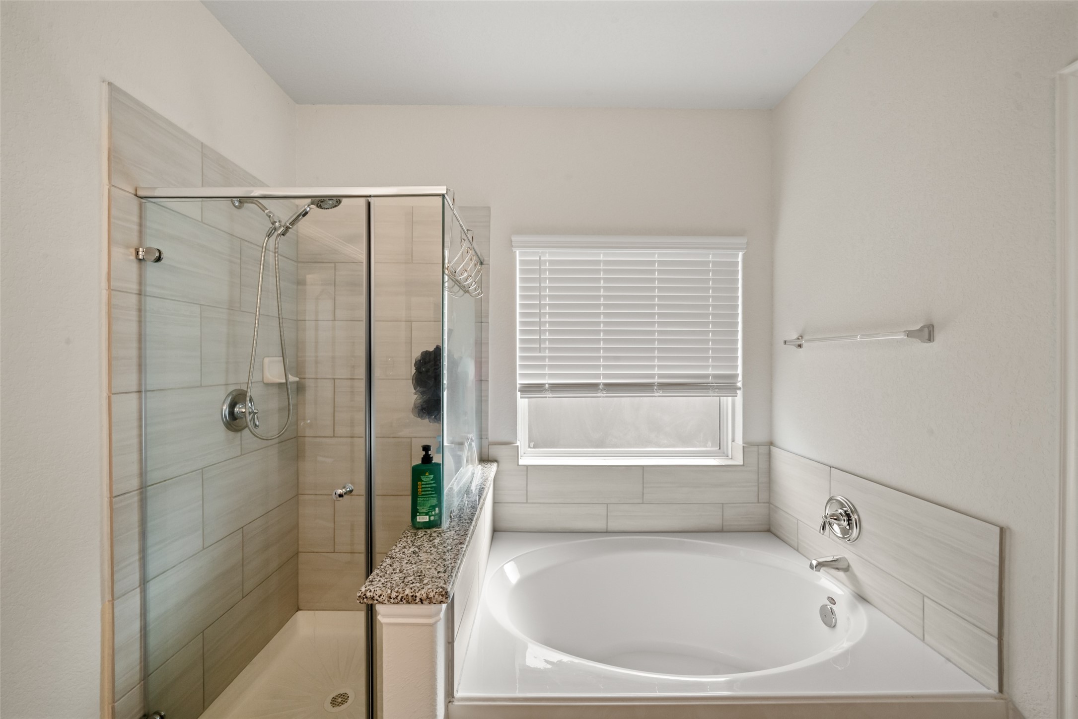 Primary bathroom featuring a sleek glass-enclosed shower and a spacious bathtub, complemented by elegant tile work and natural light from a large window.