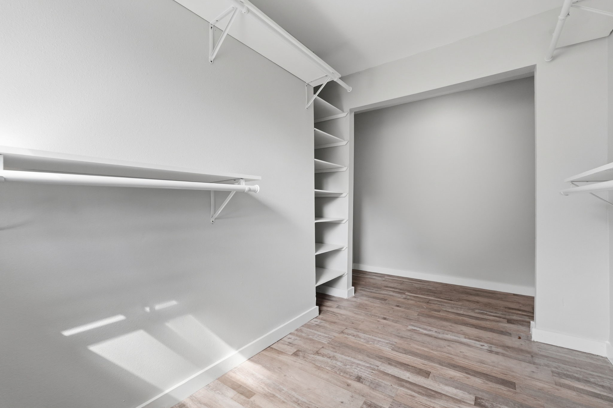 This walk in closet offers plenty of shelving and hanging space, complemented by natural light.