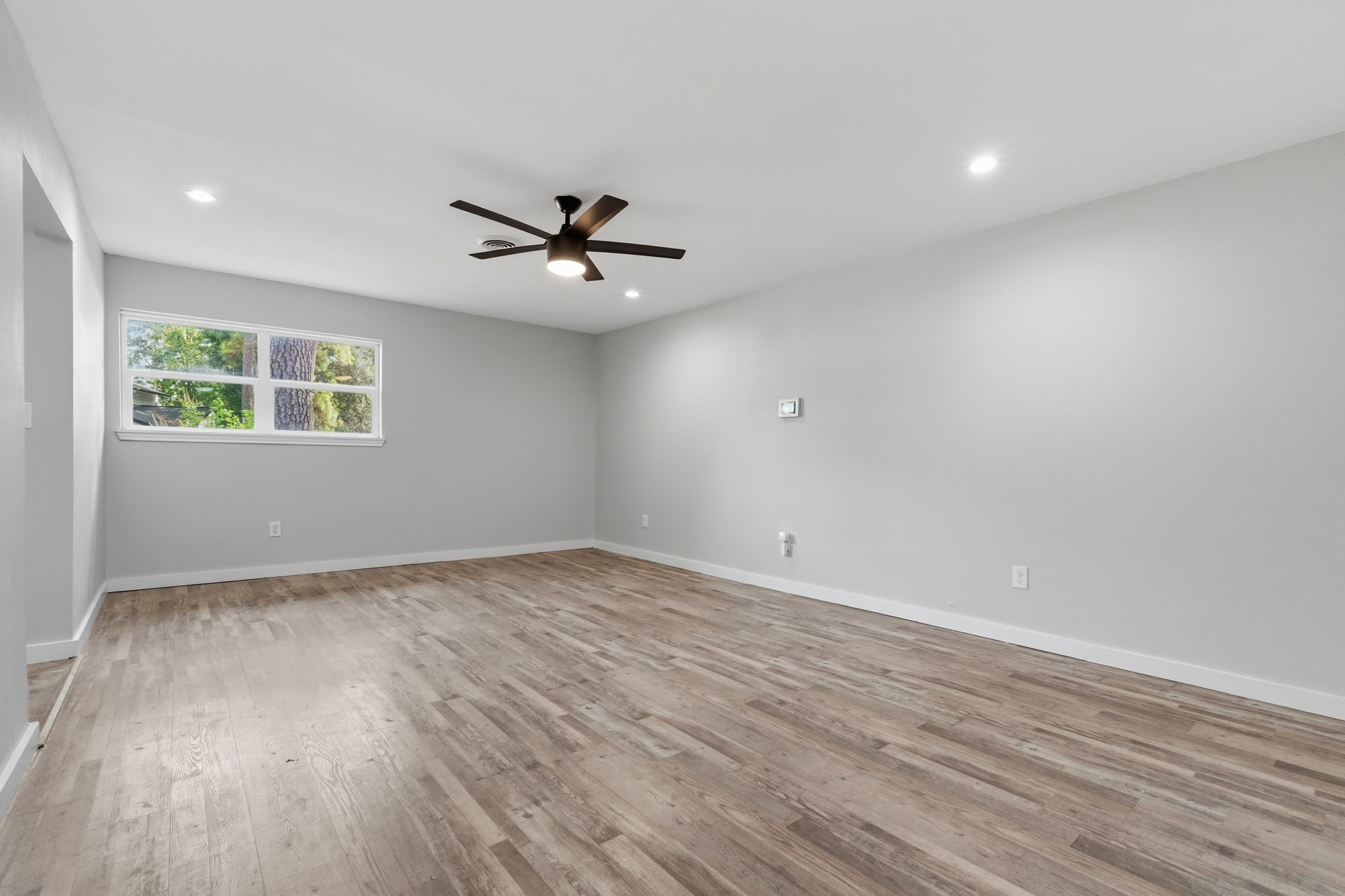 A large primary bedroom with sleek hardwood floors, large window for natural light, and a modern ceiling fan for comfort.