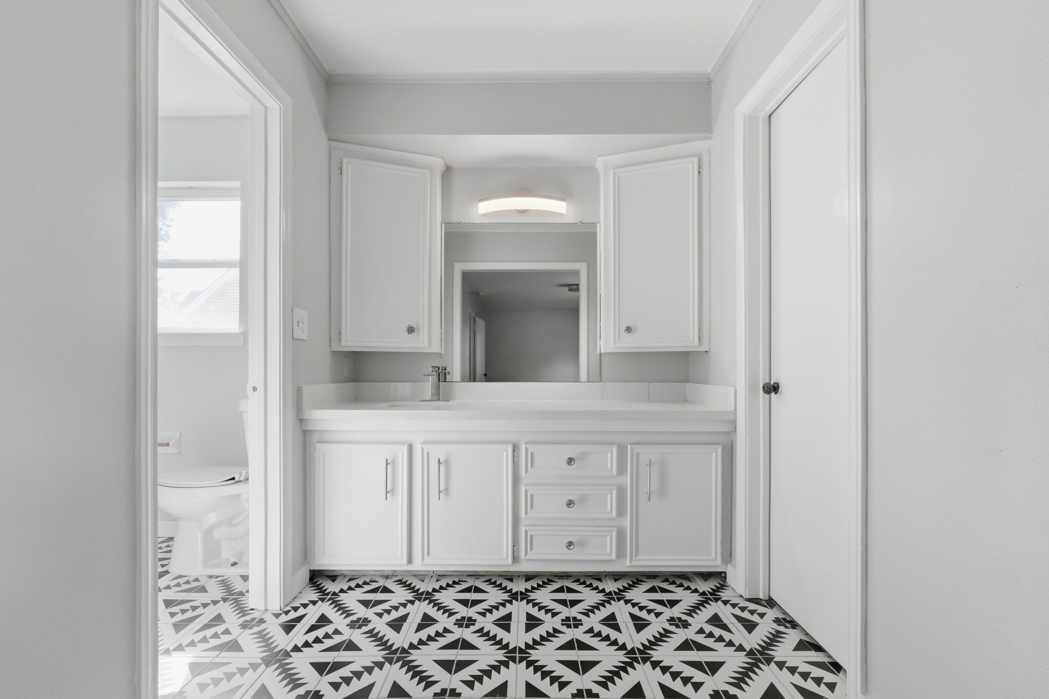 Bright bathroom featuring a sleek white vanity with ample storage, illuminated by modern lighting, and newly furnished tiles.