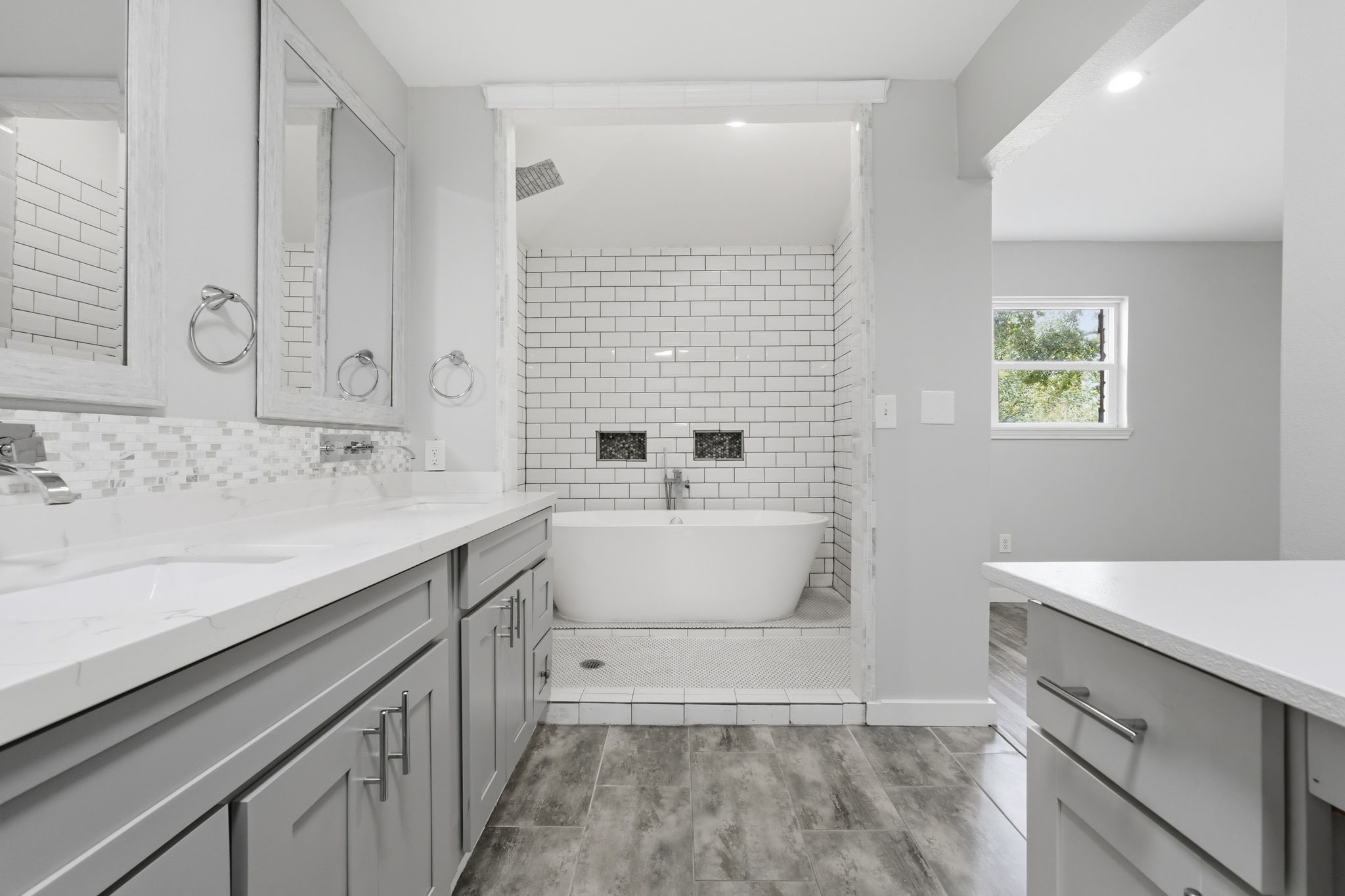 This luxurious bathroom features a freestanding, soaking bathtub framed by elegant white subway tiles and a large rainfall shower.